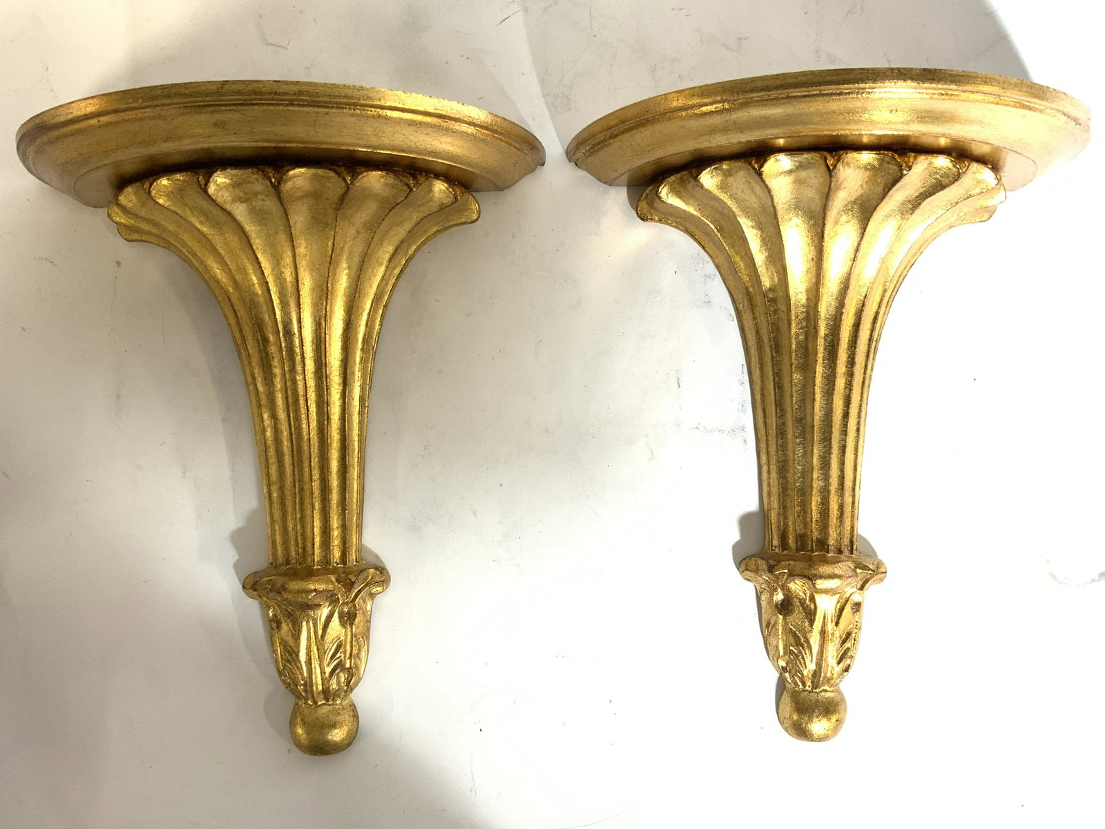 Pair DECORATIVE CRAFTS INC Giltwood Wall Shelves: Lot includes 2 wall mount shelves. Each appear to be gilt wood. Shelves have ornate detail. Shelf platforms have half circle shape. Each piece measures approx 11 inches tall 10 inches wide. Wall shelv