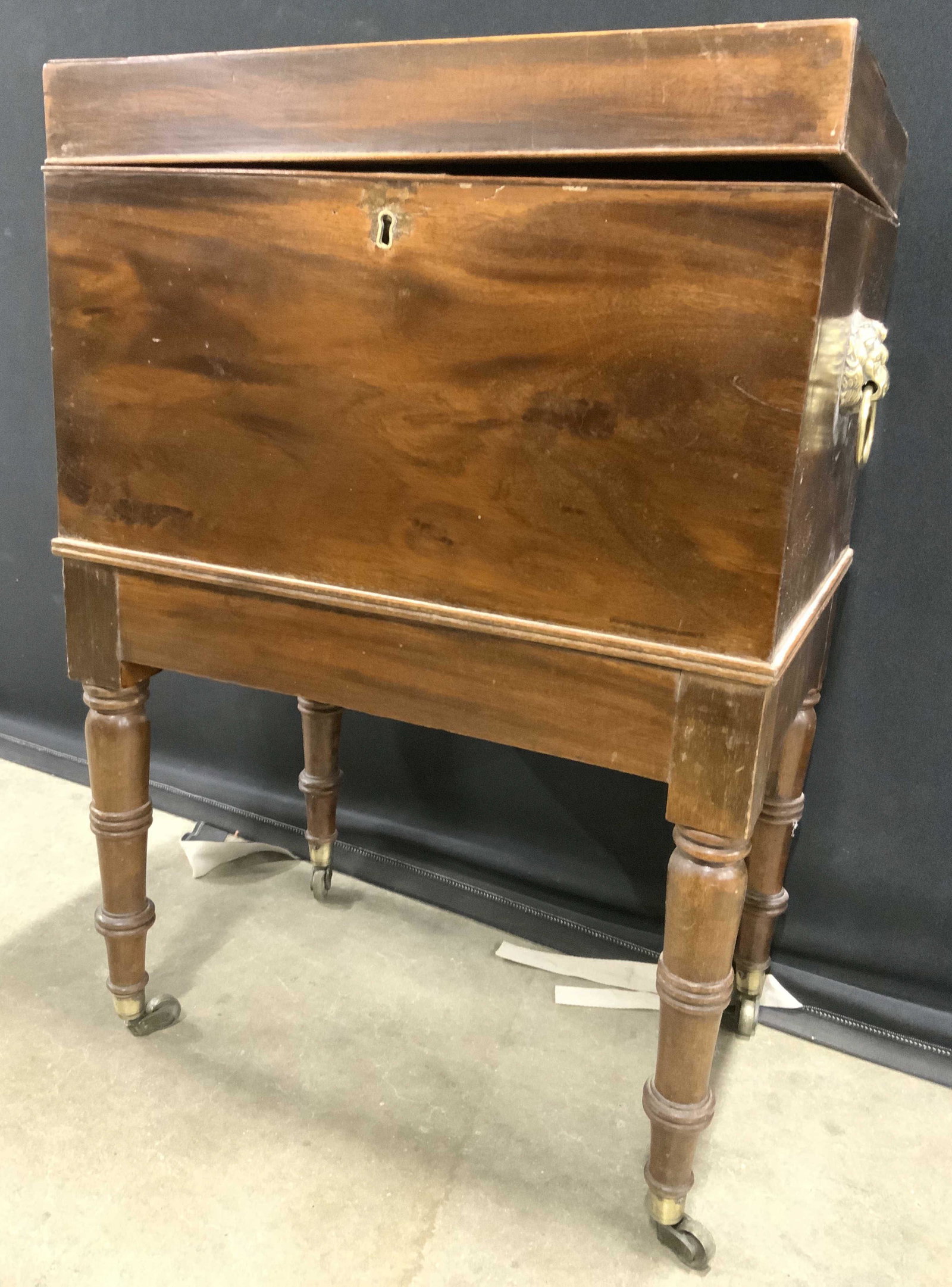 Antique English Wooden Cellerette: Cellerette is antique. Piece is wooden carved legs and brass caster feet. Each side has brass lion head handle. Piece has keyhole. Top of piece has flip open lid with 6 sections. Piece measures approx