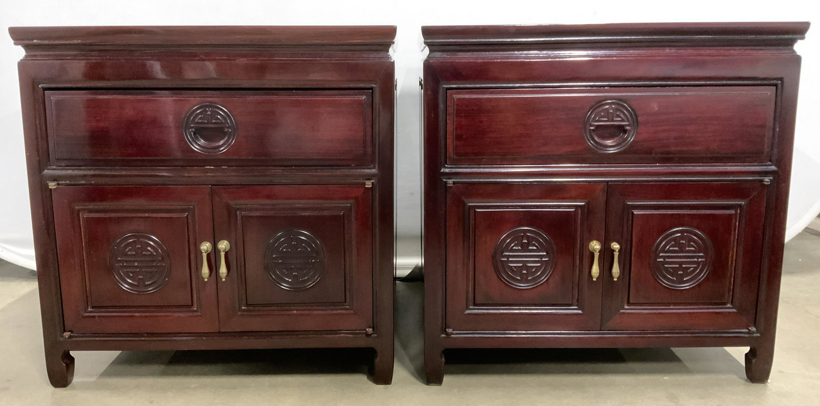 Pair Of Chinese Rosewood Side Tables: Side tables are Chinese rosewood. Each have 1 drawer and cabinet doors which open to storage area. Each have carved wooden medallion detail on drawer and cabinet doors. Each measures approx 22 inches 