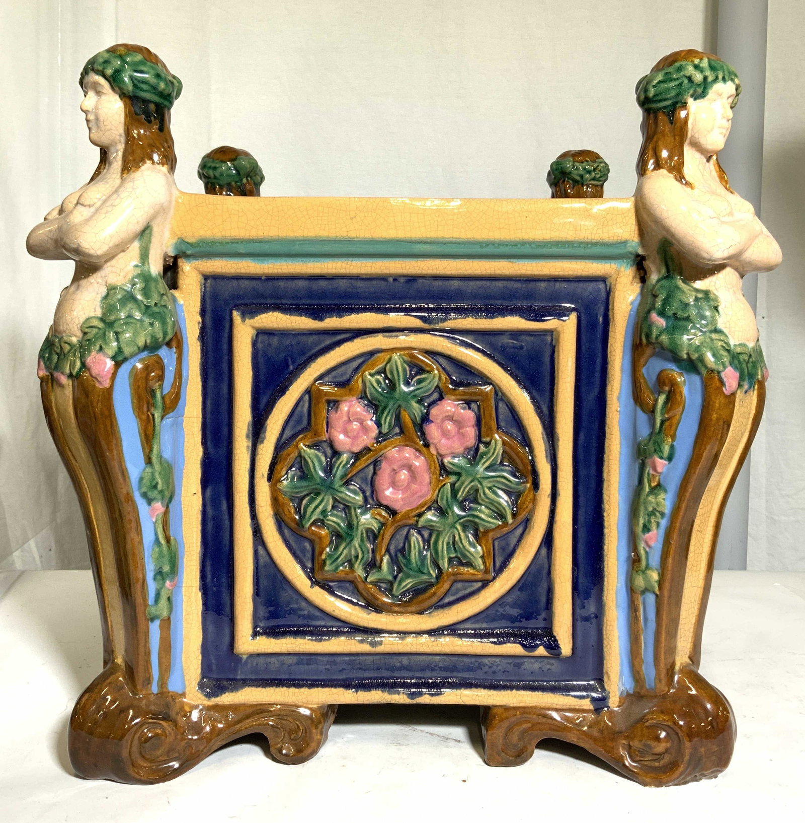 Minton Style Planter W Female Nude Figures: Planter is ceramic. Piece has 4 female nude figures in corners of structure. Each side of planter has beveled multi toned floral and leaf detail. Each corner has brown toned ornate s scroll style feet