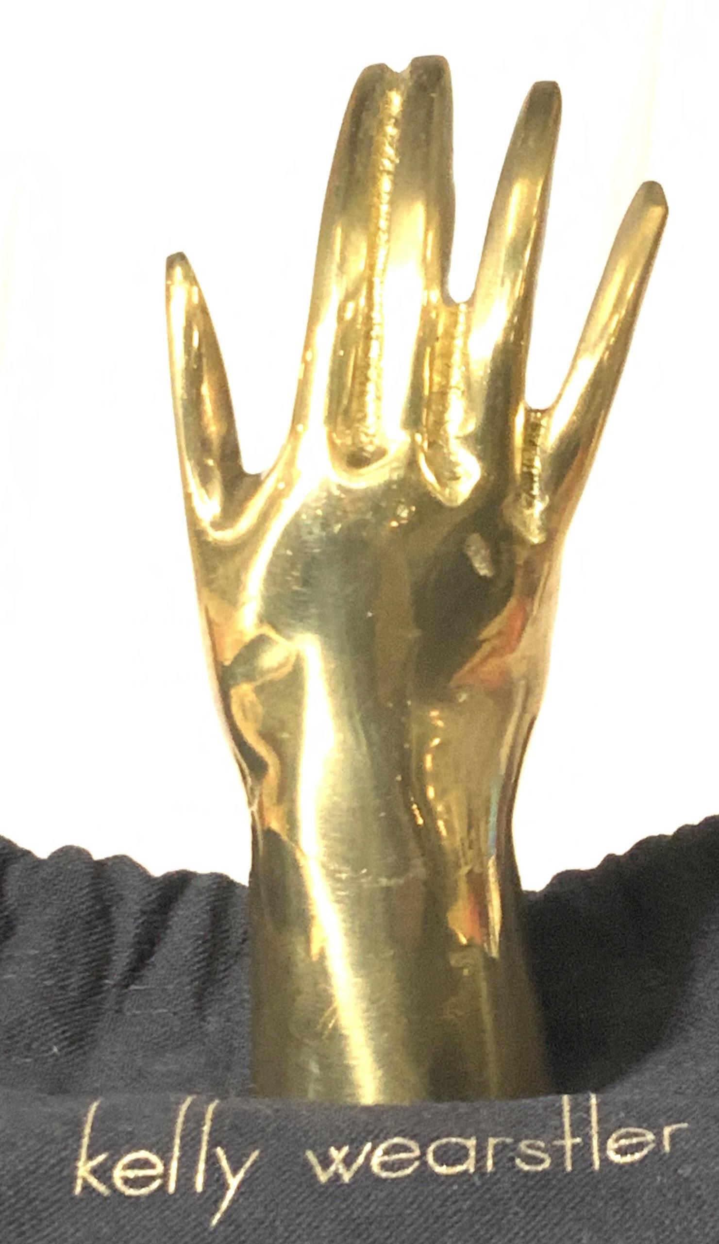 KELLY WEARSTLER Brass Hand Form Sculpture, Bag: Luxury Brass sculpture with duster bag labeled Kelly Wearstler. Sculpture of hand with pointer and middle finger together. Can use as a ring holder or solely as a decorative object. 5 in. Ht. 1.75 in 
