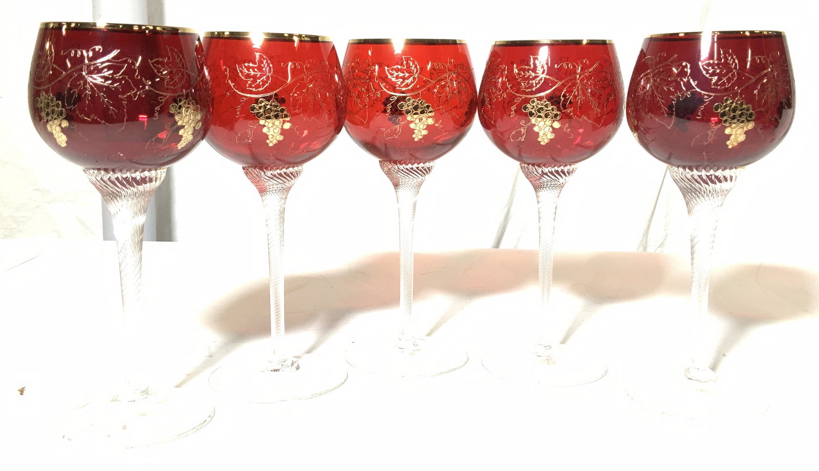 Set 5 Crystal & Gilt Stemware Goblets: Ruby red crystal goblets accented with hand painted gilt grape vine decor, twisted stem adds to the distinct look. Gilt rim, etched with gilt and solid painted grape bunch gilt. 8 in ht, 3.5 in width.