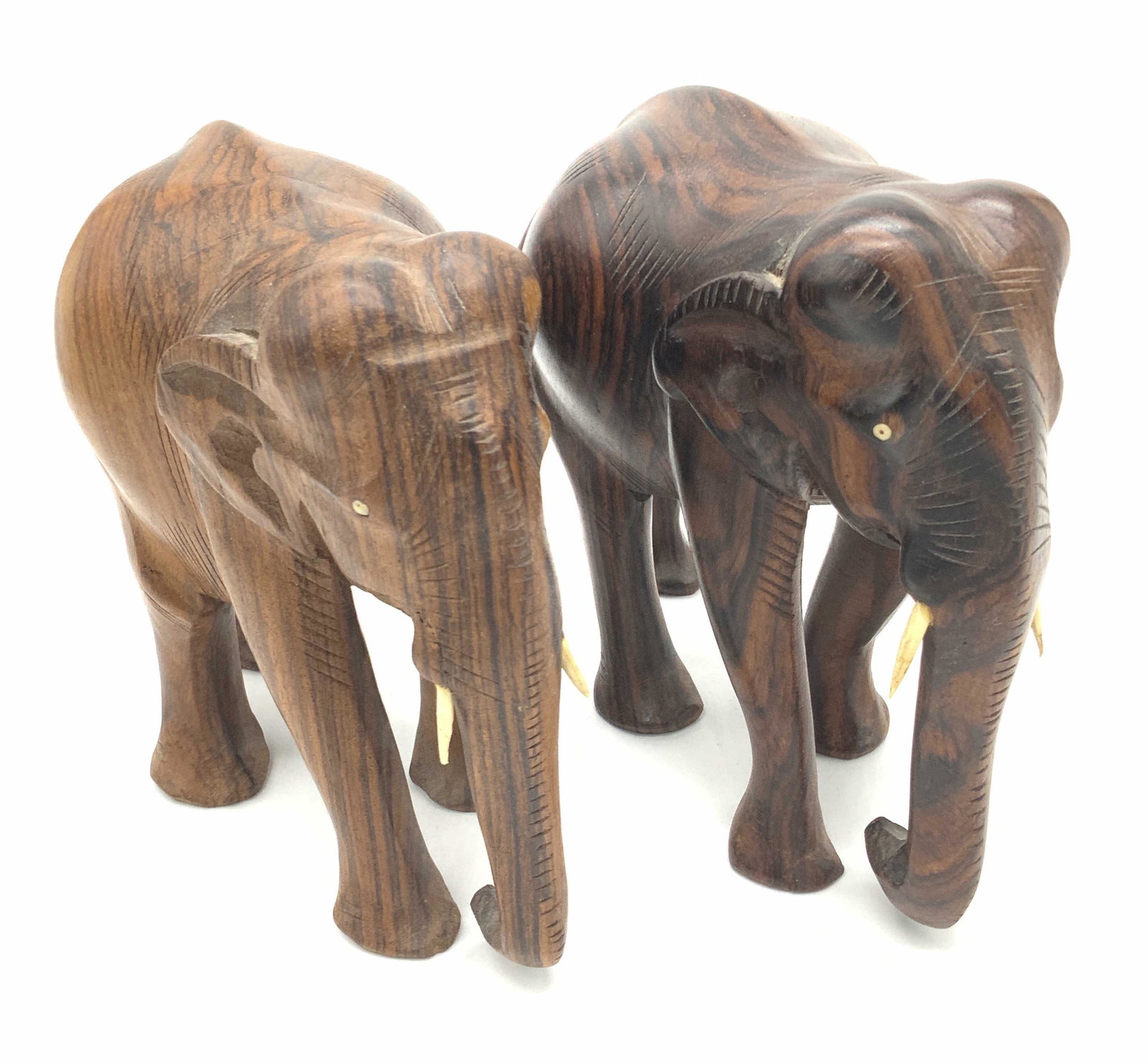 Pair Carved & Etched Wooden Elephant Figurals: Two carved and etched wooden elephant figurals. Both pieces crafted from brown hued wood. Striations visible in both pieces. Tusks are carved from a lighter hued wood. Pieces are similar in size. Appr