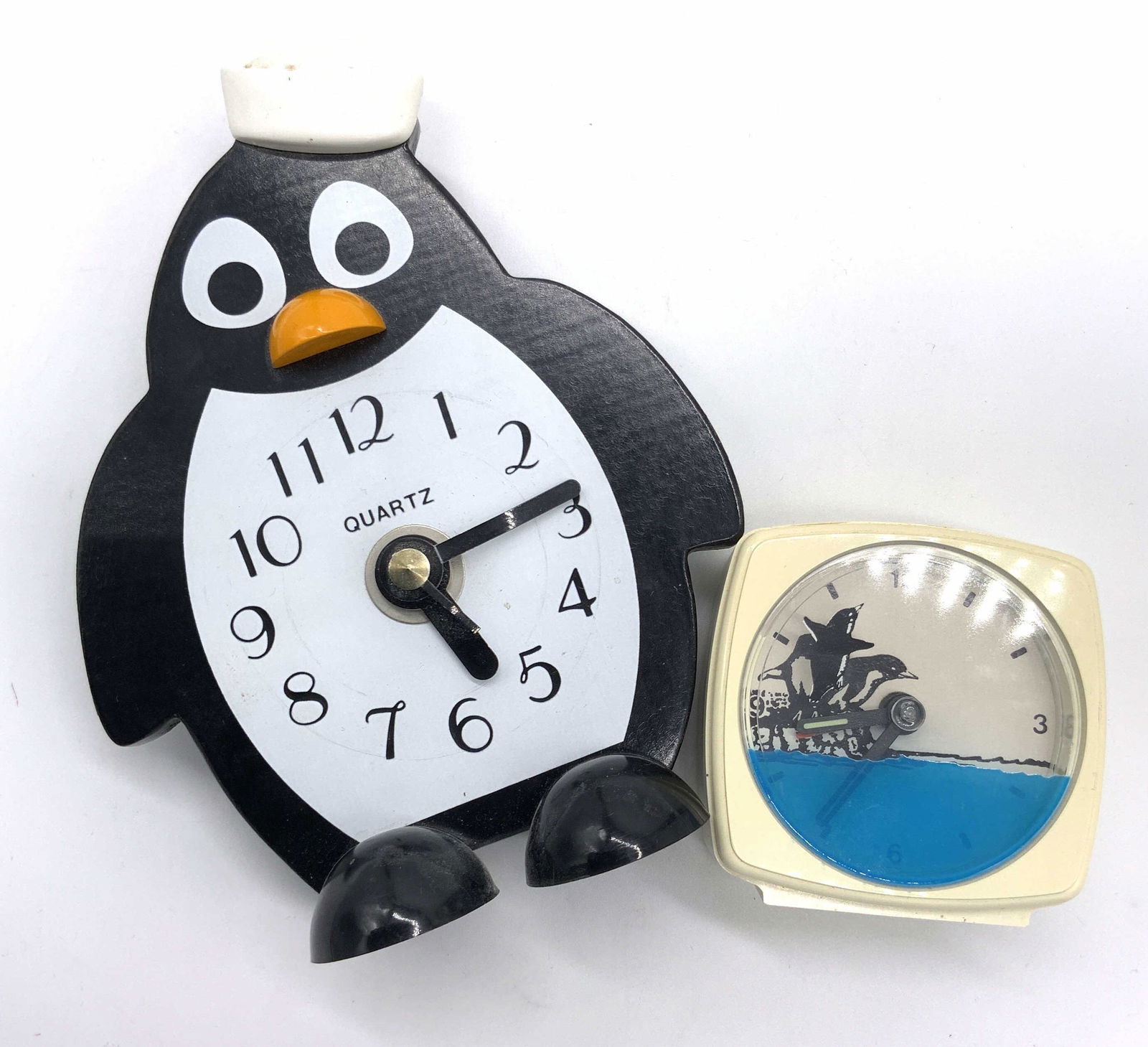 Lot 2 Collectible Penguin Motif Tabletop Clocks: Two composite Penguin motif tabletop clocks. Pieces are possibly vintage. The larger of the two pieces is a Penguin form wearing a sailor’s face. The clock face is on the Penguin’s stomach. On the