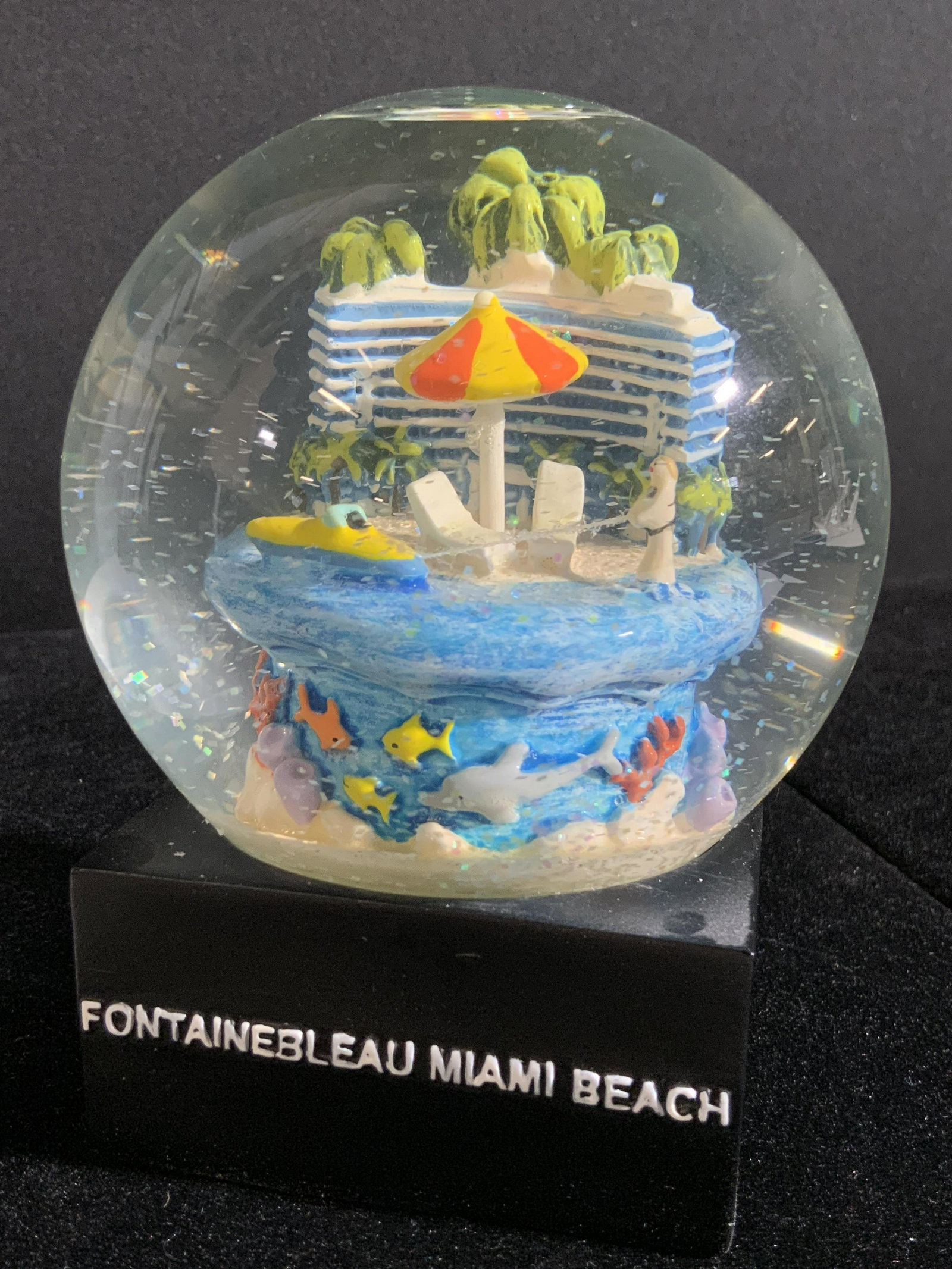 Limited Edition FONTAINEBLEAU Miami Snow Globe: A collectible glass and composite snow globe filled with liquid and glitter. Once shaken, the glitter swirls about around a figural depicting Miami’s Fontainebleau. Obverse reads FONTAINEBLEAU MIAMI