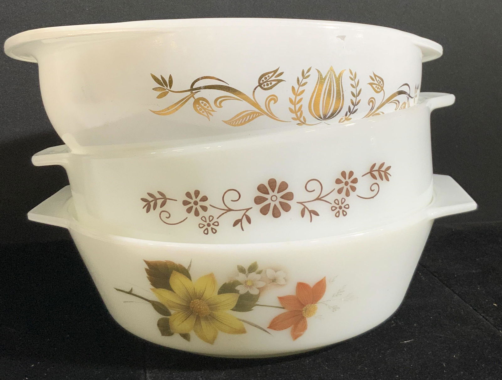 Lot 3 Vntg Floral PYREX Trademarked Ovenware Bowls: Three vintage Pyrex bowls. All bowls are primarily white with floral details. Floral details possess gilt hues and earth toned hues. Undersides read PYREX, OVENWARE, MADE IN ENGLAND / MEXICO / USA. On
