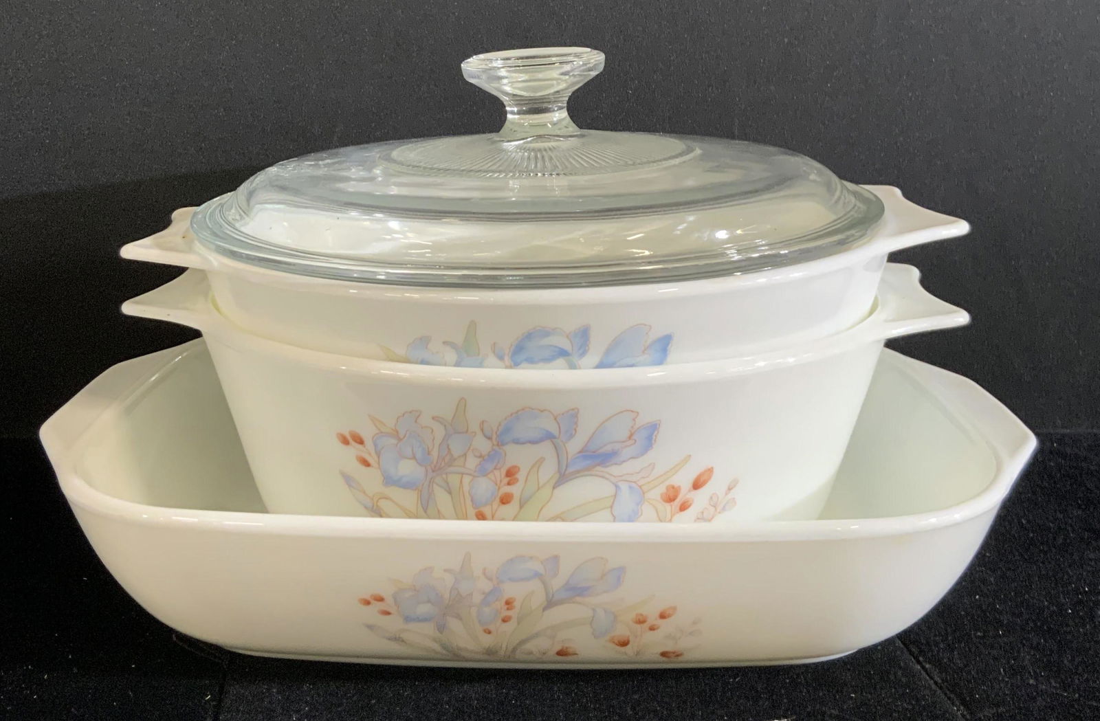 3pc PYREX English Blue Iris Pattern Dishes: Three vintage white Pyrex baking dishes. Each piece features the blue iris pattern. All pieces are handled. Undersides read PYREX, ENGLAND Largest bowl approx. 3H x 10.5W in. Varying sizes. One piece
