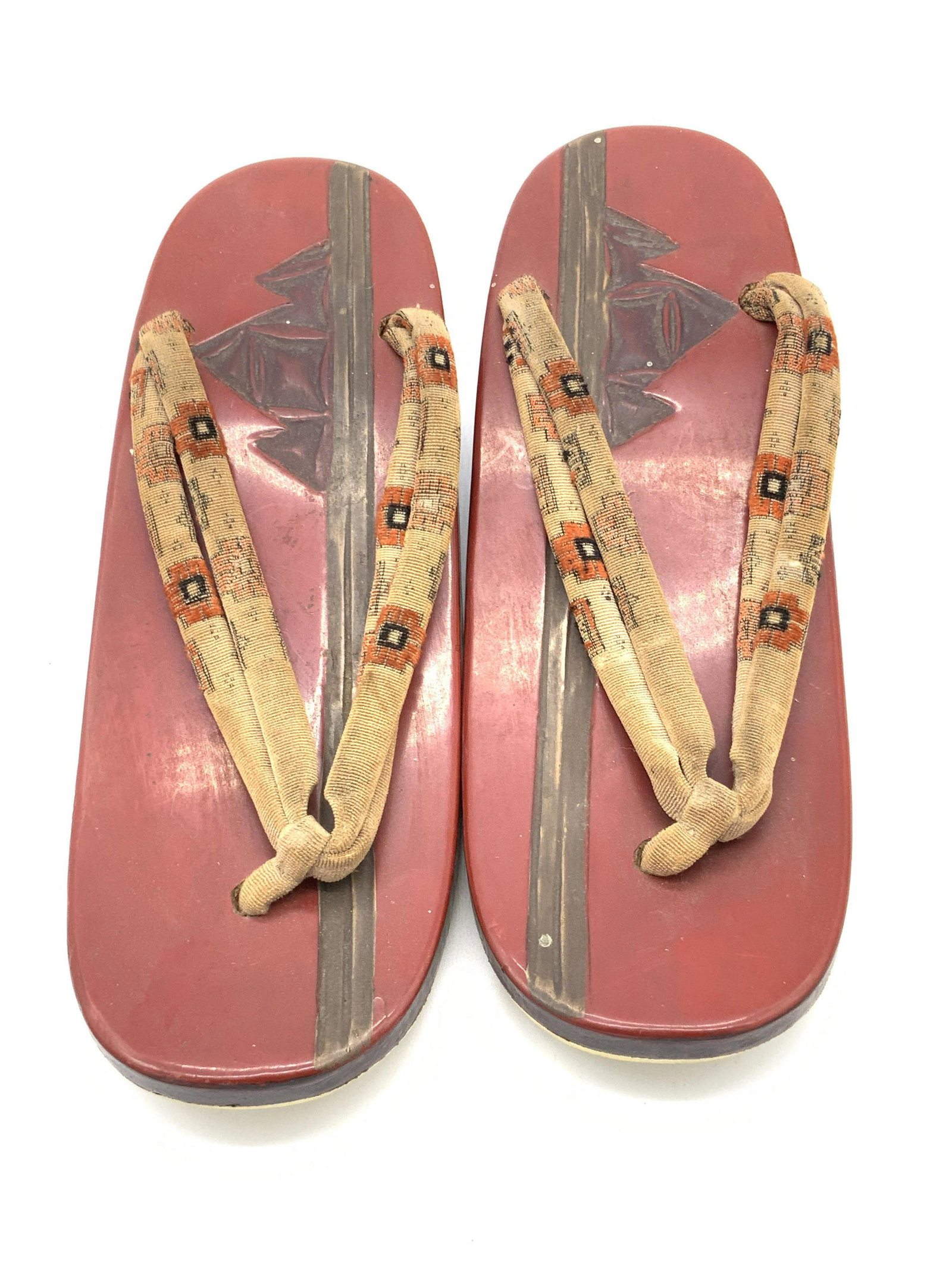 Vintage Traditional Japanese Footwear, Geta: A vintage pair of Japanese Geta. Pieces are crafted from wood and lacquered red. Primarily red with earth toned hues. The straps are a patterned fabric material. Designs depict mountains. Some wear co