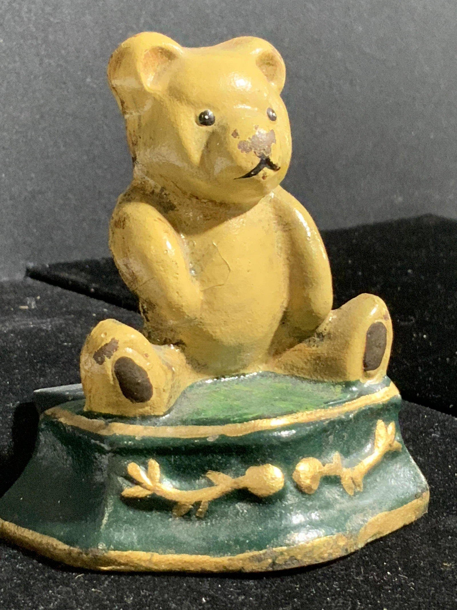 Vintage Hand Painted Iron Bear Form Doorstop: A vintage, possibly antique, iron bear form figural doorstop. The piece features a beige hued bear sitting atop a green base with gilt toned line work. Piece has some evident wear to metal and paint c