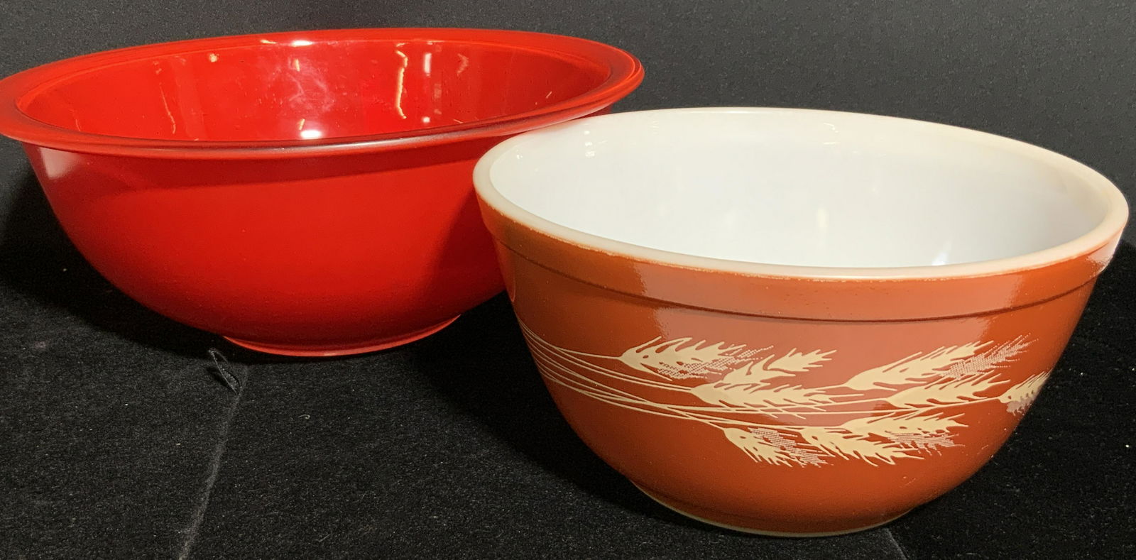 Lot 2 Vntg PYREX Trademarked Ovenware Bowls: Two possibly vintage Pyrex bowls. Pieces are red and orange hued. One features a wheat stalk design. Underside reads TRADEMARK PYREX, USA, FOR OVEN. Larger bowl approx. 4H x 9.5W in. Both pieces featu