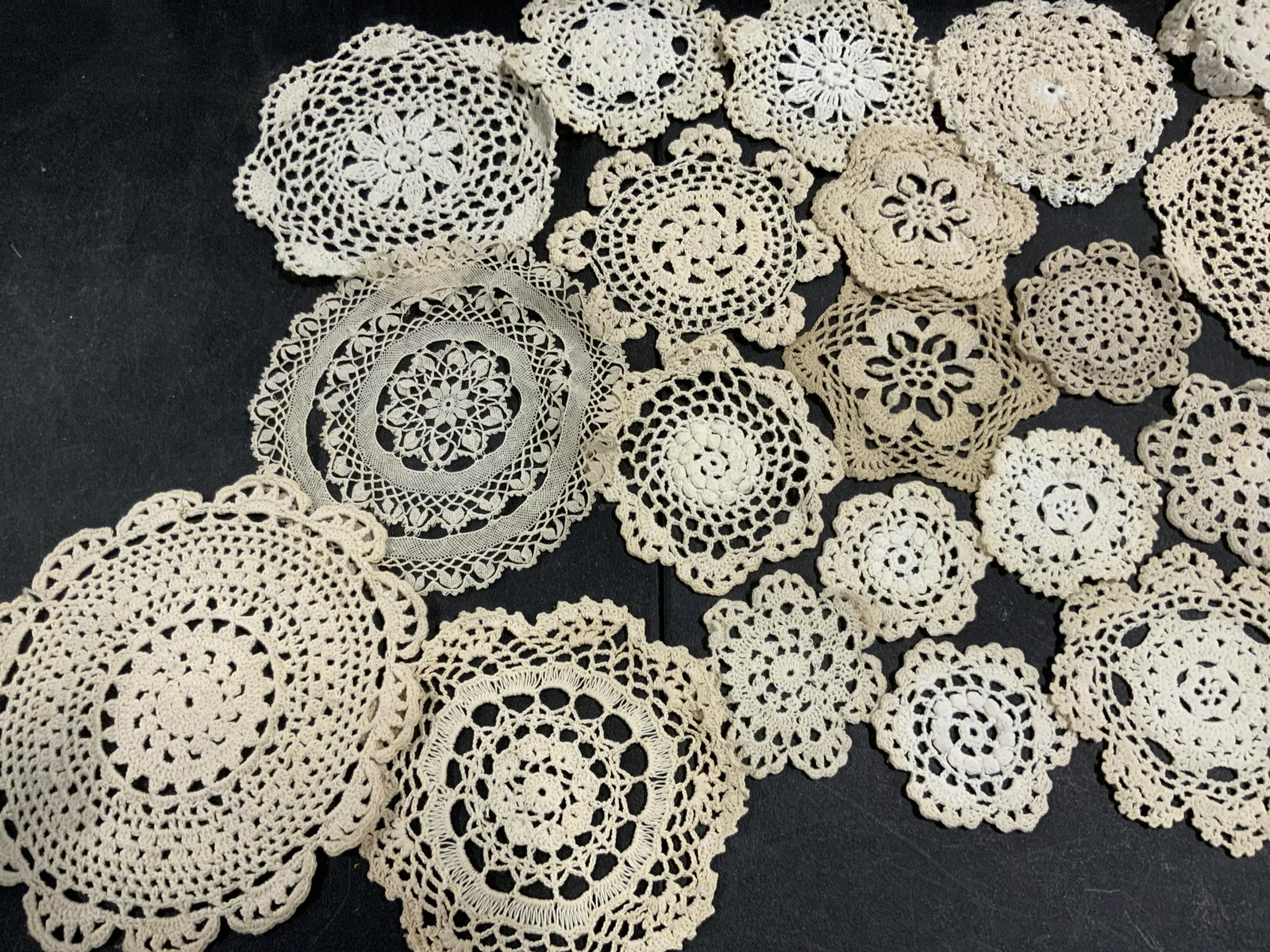 Lot 28 Handmade Vintage Crochet Doilies: A lot of 28 vintage handmade doilies. The pieces are circular, snowflake, and star forms. Pieces are primarily beige hued. Varying sizes. Largest Approx. 8 x 8 in. One piece appears to be crafted from