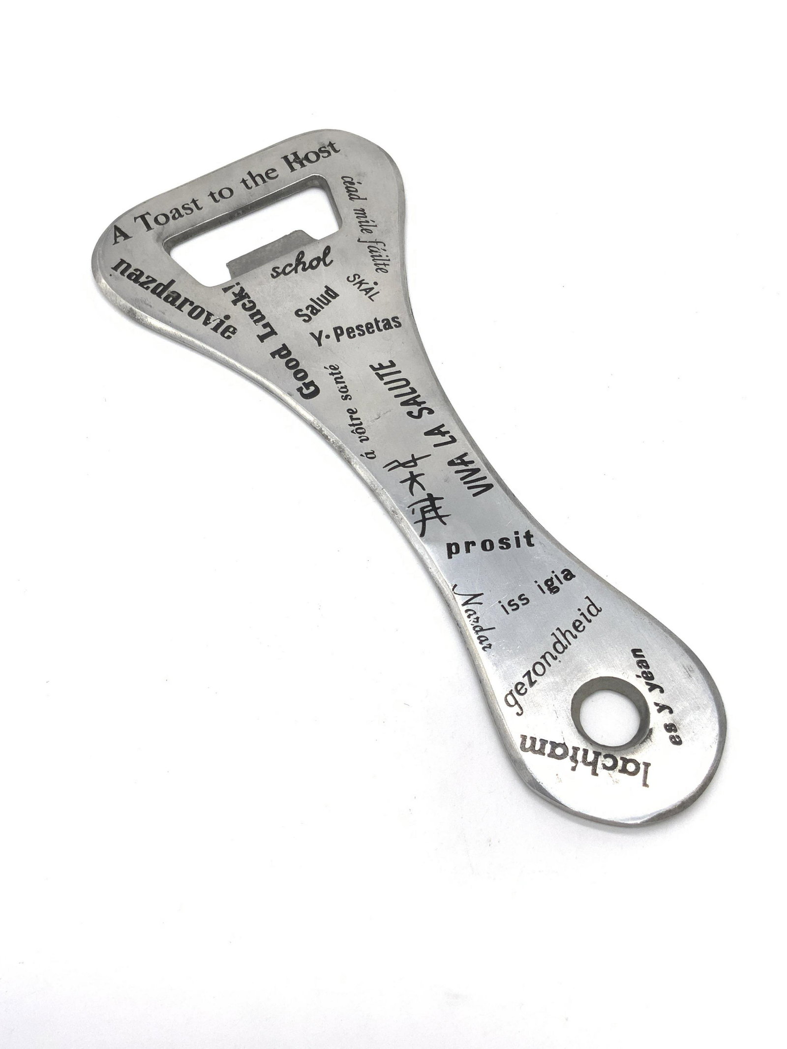 Oversized Italian Metal Bottle Opener: An oversized silver tone metal bottle opener. The obverse has numerous sayings in foreign languages and English. The underside reads MADE IN ITALY. Approx. 9.5L x 4W in. He’s had some surface wear. 