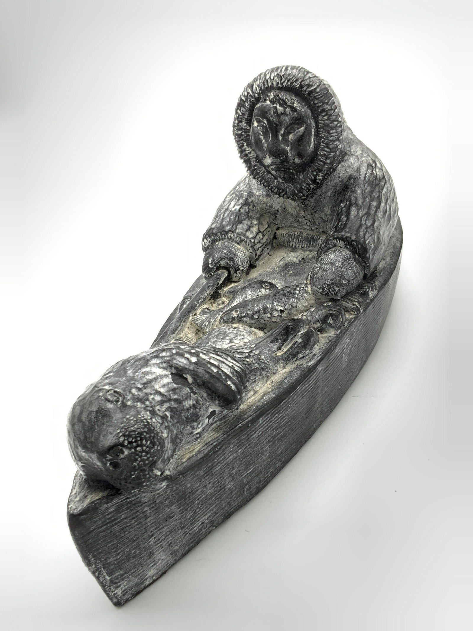 Hand Carved Soapstone Inuit Nuvuk Figural, Canada: A handmade carved and etched figural depicting an Inuit within a boat. At the other end of the boat there is a walrus, in the center there are fish. All pieces are precisely carved and etched from nat