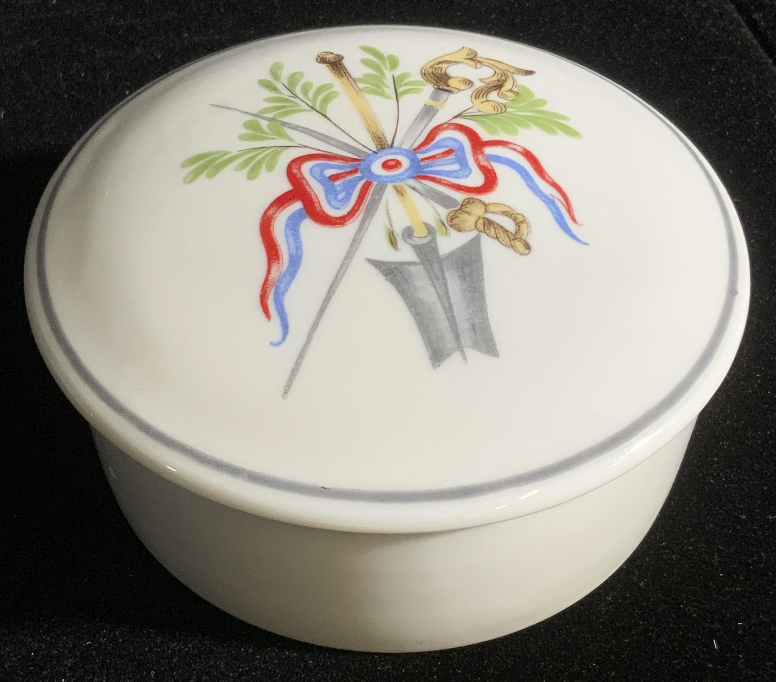 LIMOGES France LANCÔME Paris Porcelain Trinket Box: A hand painted white porcelain lidded trinket box. The lid features laurels, ribbons, and swords. The interior is white. The underside reads DECORATED FOR LANCÔME PARIS BY MNP FOR LIMOGES FRANCE, BIC