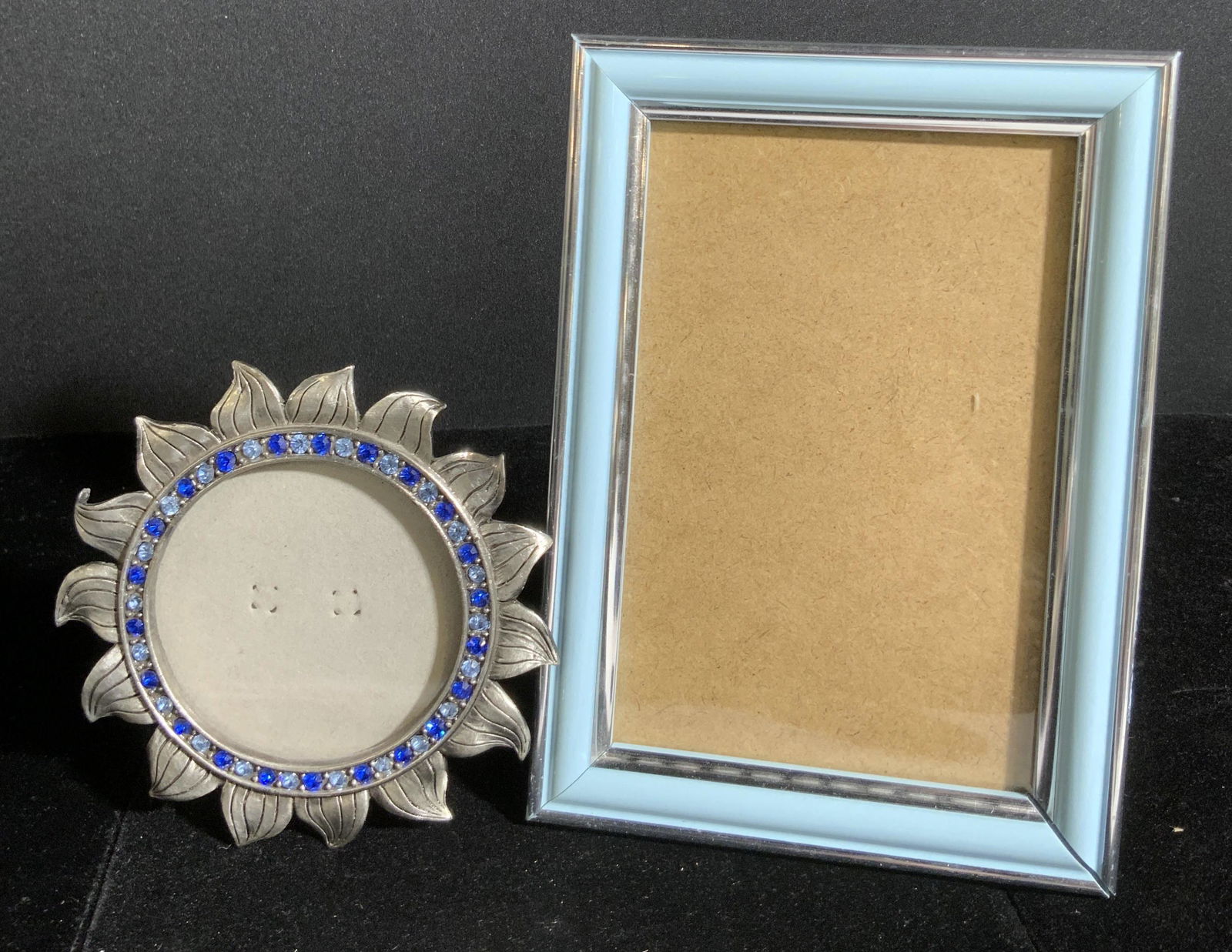 Lot 2 Blue Hued Metal Picture Frames: Two blue hued metal picture frames. One piece is rectangular in shape and has both silver and blue hues. Approx 7H x 5W in. The other frame is circular in form and made to resemble the form of the sun