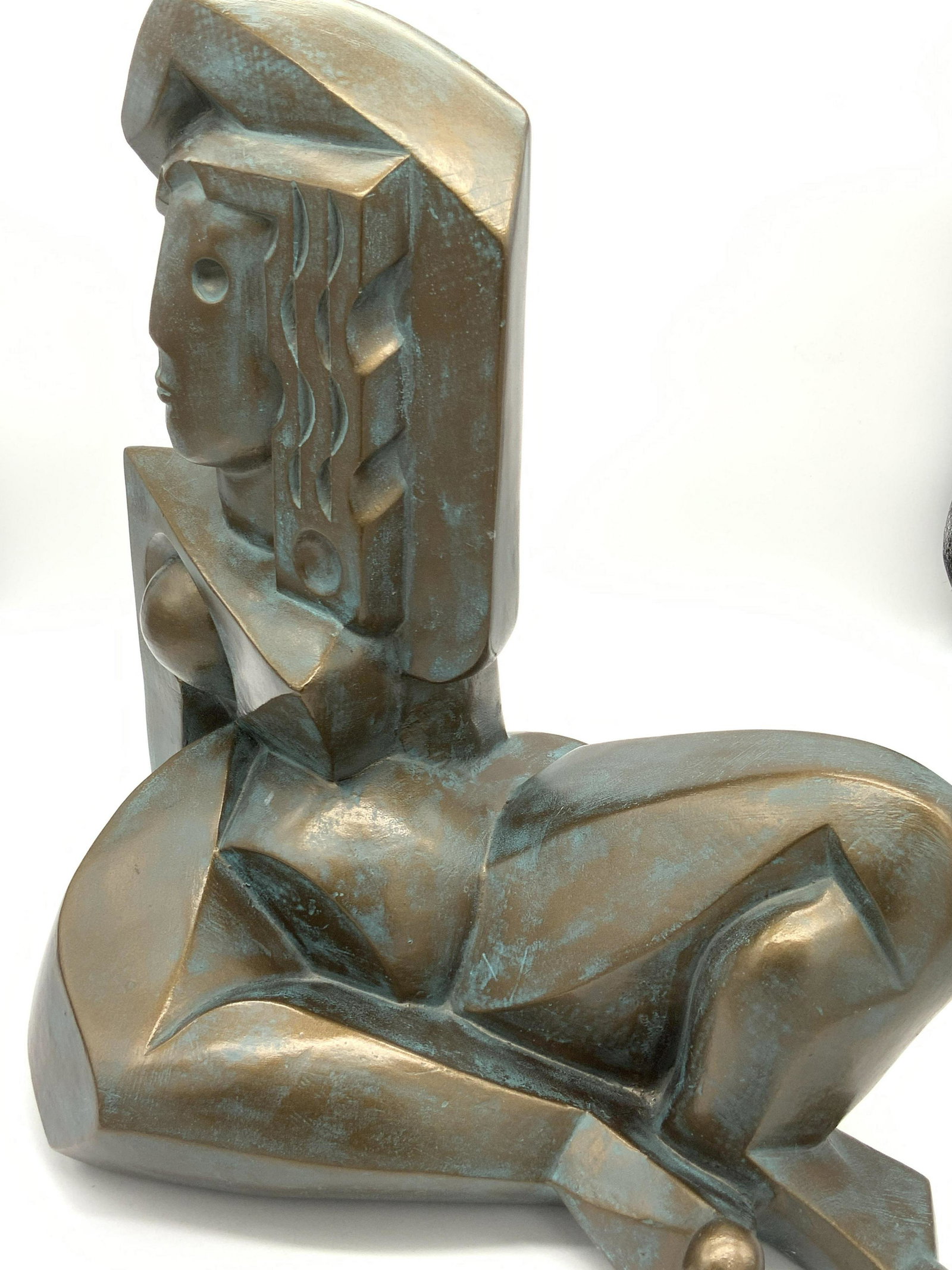 Art Deco Cubist Nude Female Form Metal Sculpture: A metal cubist sculpture depicting a nude woman. She has one arm draped over her head, the other is supporting her. She is seated with both legs bent. The metal is a brushed bronze hue with accents of