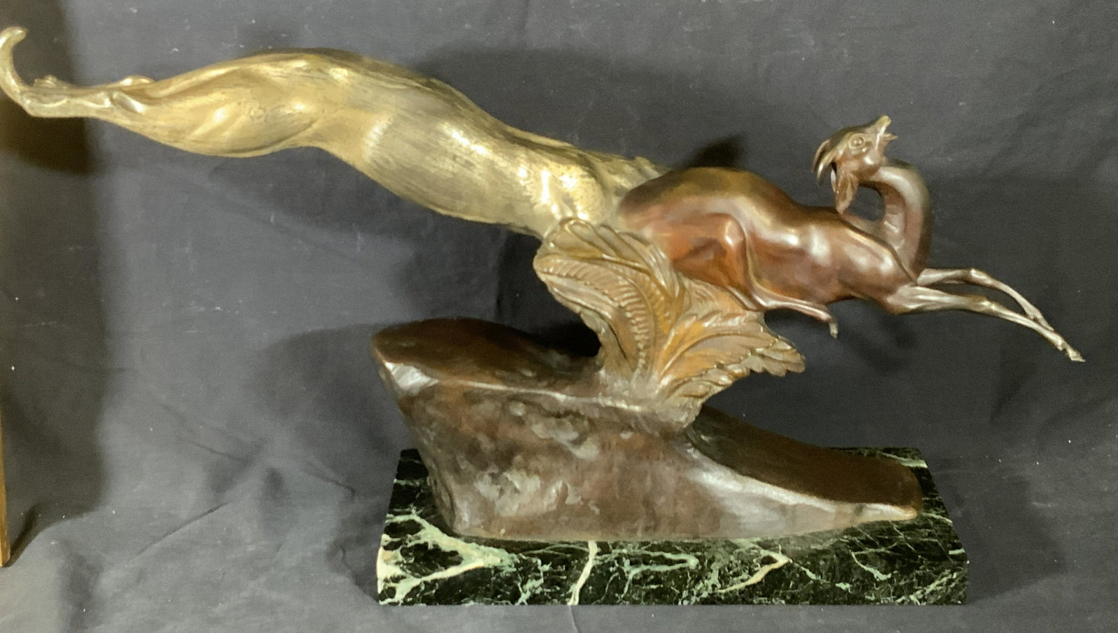 FRAMCISQUE MECLAILLEDOR Signed Bronze Sculpture: A sculpture comprised of both metal and natural stone. Appears to be crafted from bronze and marble. The piece depicts a lion hunting a gazelle. Gilt bronze and painted bronze accents. Etched and embo