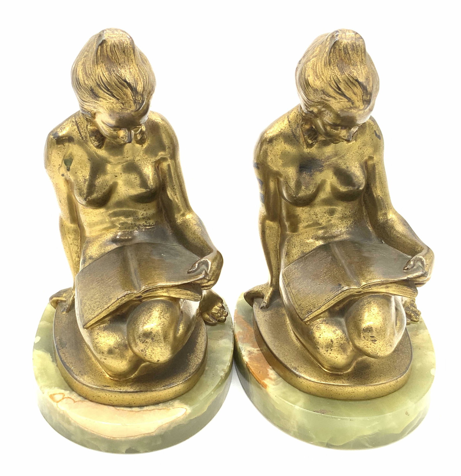 Pair Gilded Metal Nude Female Figural Bookends: A pair of bookends crafted from metal, possibly bronze, and natural green stone. The metal is crafted into the form of a nude woman. She is seated and reading a book. She is affixed to the polished na