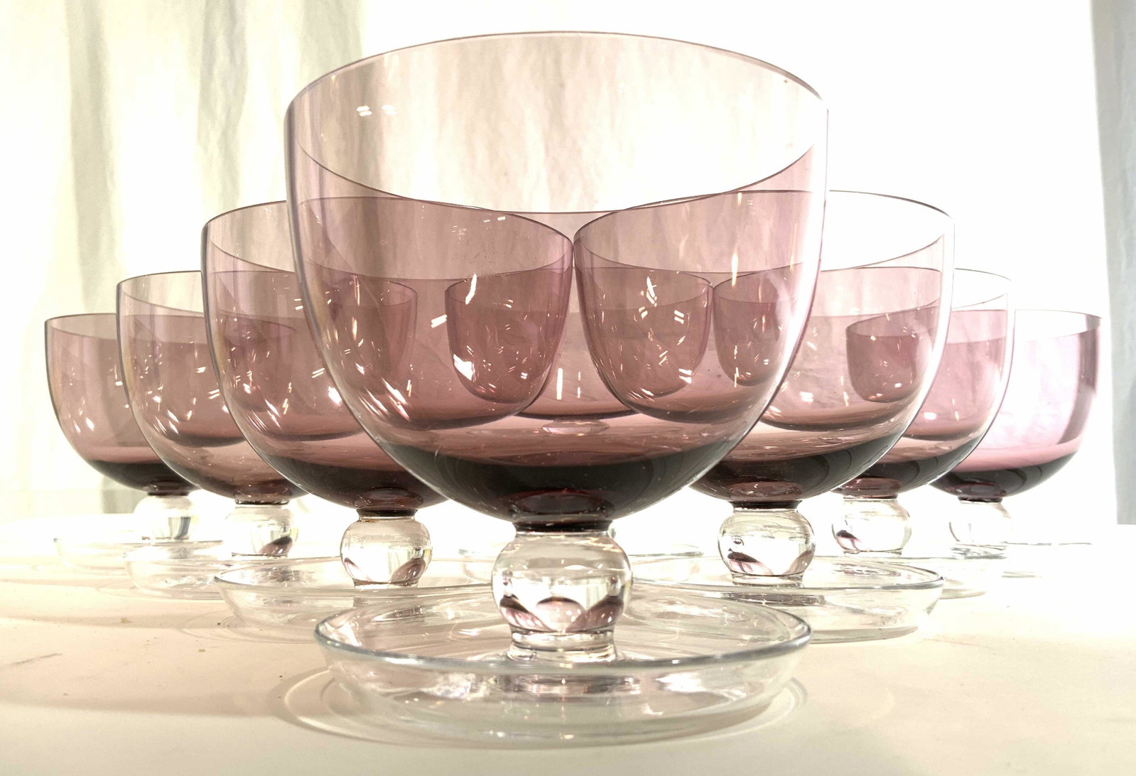 Set 8 Short Stem Wine Glasses: Wine glasses are purple toned with clear stems. Stemware Is possibly crystal. Base of stems resemble saucers. Each piece measures approx 4.75 inches tall & wide. Stemware, purple stemware, wine glasse
