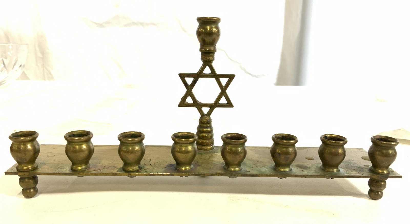 Gold Toned Brass Judaica Menorah: Menorah is gold toned. Piece appears to be brass. Piece has Star of David in center of piece. Menorah is footed. Piece measures approx 8 inches long 4 inches tall 2 inches deep. Menorah, brass menorah