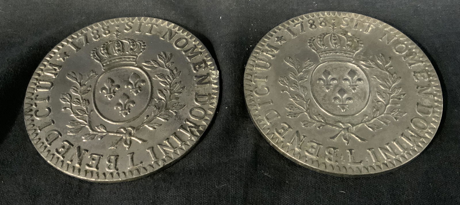 Pair Metal Latin Crest Coasters: Pair Metal Latin crest coasters, both have Latin text to their surface with the date 1788, both have a crest with a crown and 3 fleur de lis, both measure approximately 3 inches in diameter, underside