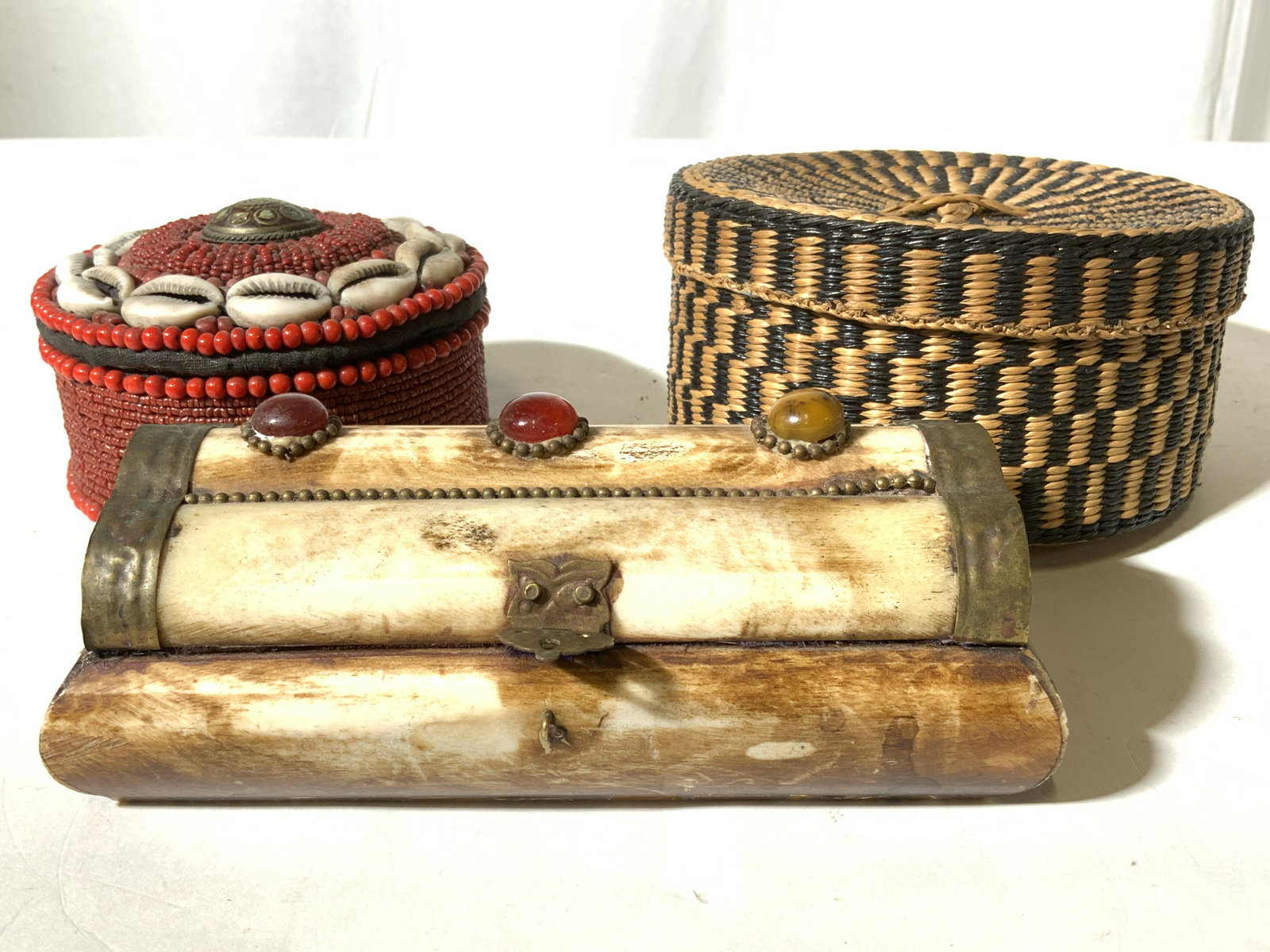 Lot 3 Assorted Keepsake Boxes: Lot includes 3 keepsake boxes. 1 woven, 1 beaded, and 1 carved bone. Each are lidded. Woven box I stand & black toned. Beaded box is red toned with shell detail. Largest piece measures approx 5 inches