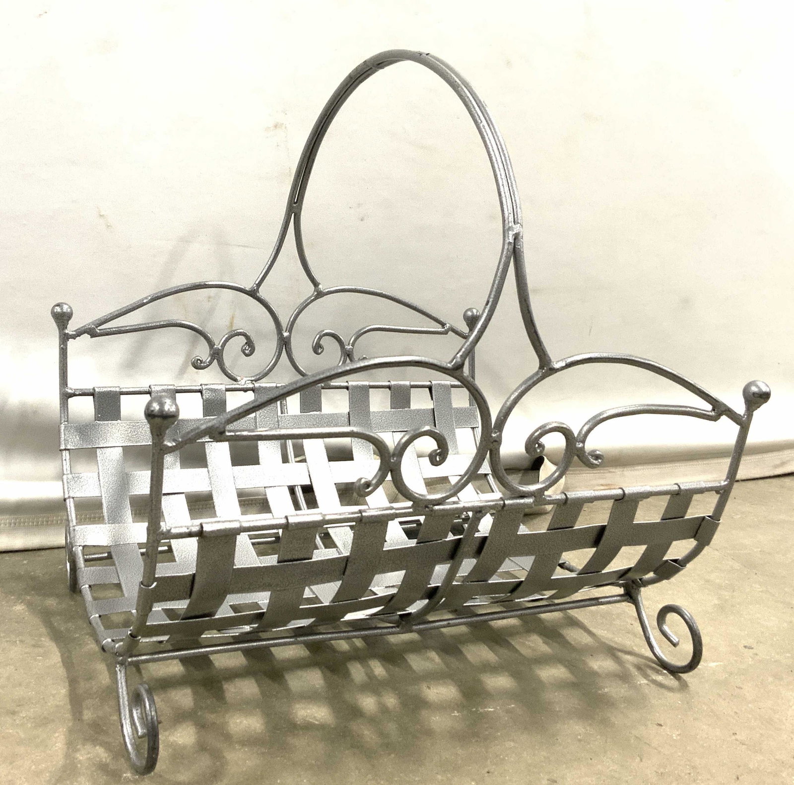 Footed Metal Firewood Holder W Handle: Firewood holder is silver toned and metal. Piece has woven metal structure. Firewood holder is footed. Piece has arched handle. Piece measures approx 14 inches tall & long 13 inches wide. Firewood hol