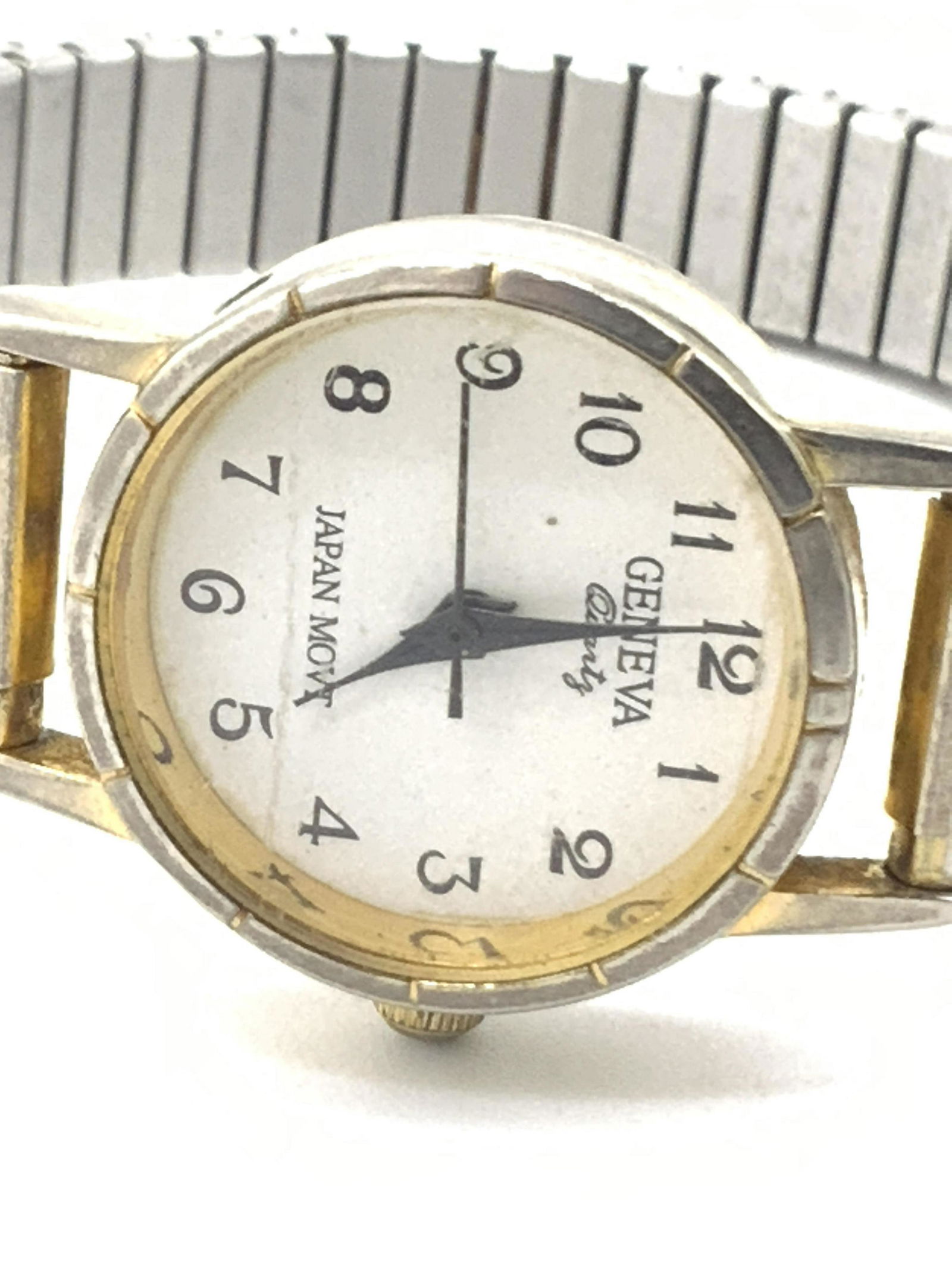Vintage GENEVA Stainless Steel Stretch Watch: A silver and gold tone metal stretch watch with a stainless steel back cover. Etched metal accents along the band. The watch face is white hued and reads GENEVA, JAPAN MOVT. The reverse reads WATER RE