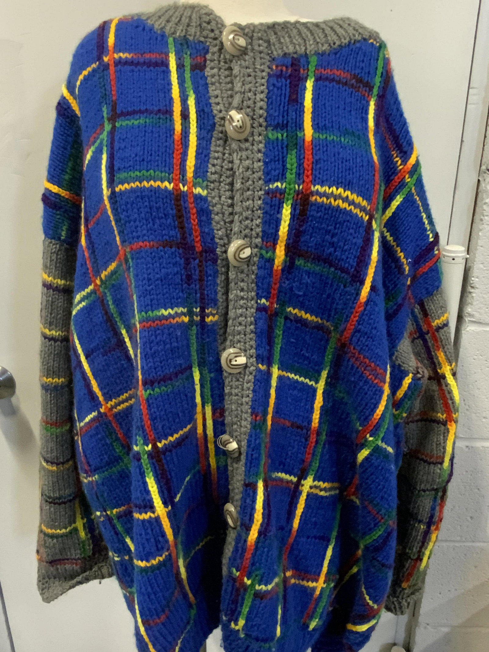 Handmade Oversized Colorful Knit Button-Up Sweater: A colorful unisex sweater. Appears to be handmade. Primarily blue and gray hued with rainbow accents. Composite buttons. Length approx. 30 in. Size approx. 2X. Some loose thread on button, some pulls,