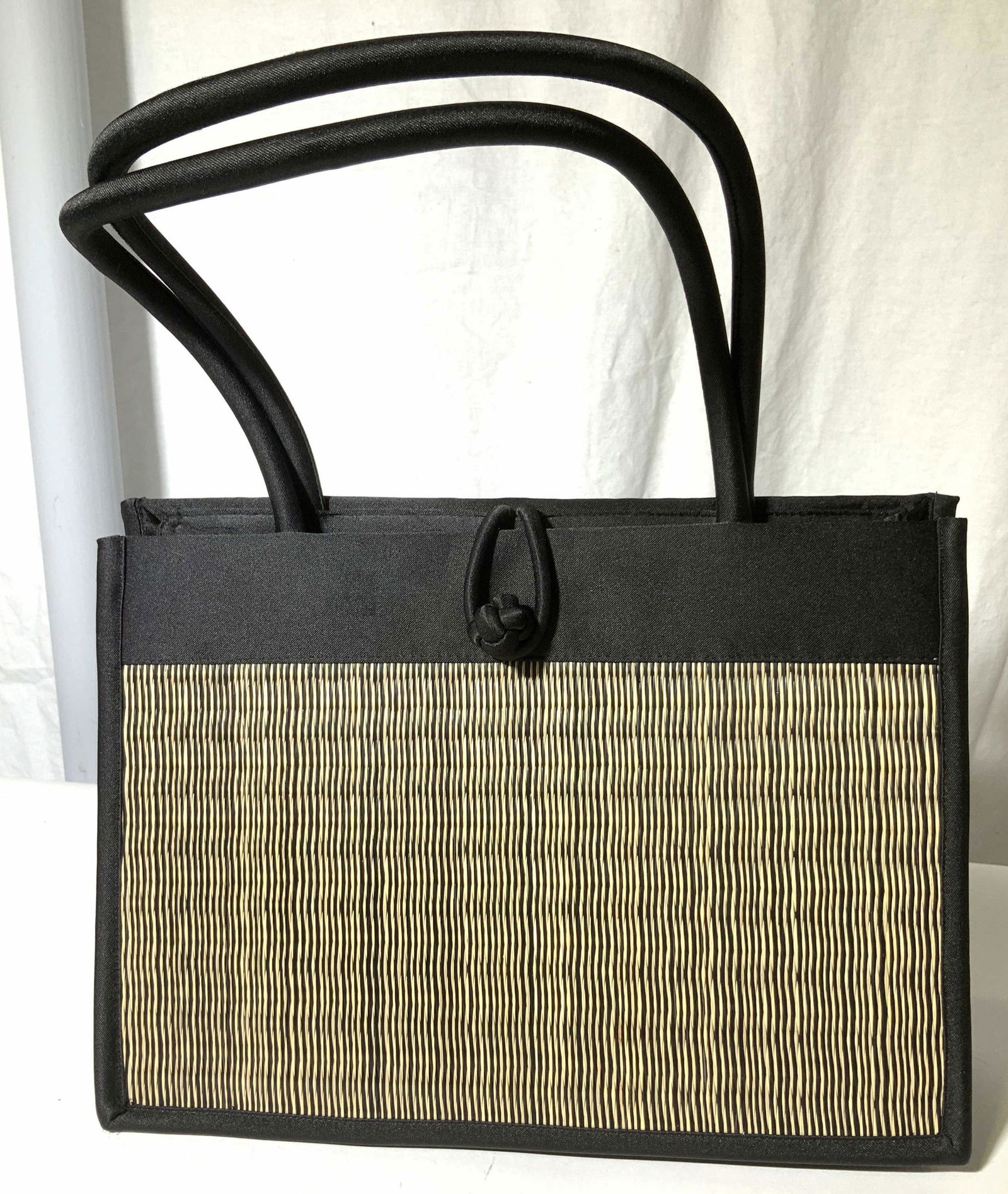 Baskets of Cambodia Top Handle Shoulder Bag: Woven grass and black sateen hard form shoulder bag, signed label Baskets of Cambodia, Asian Knot button and loop clasp, open interior with inner pockets/ pouches. Bag measures 13 x 9 x 3.5 in. Basket