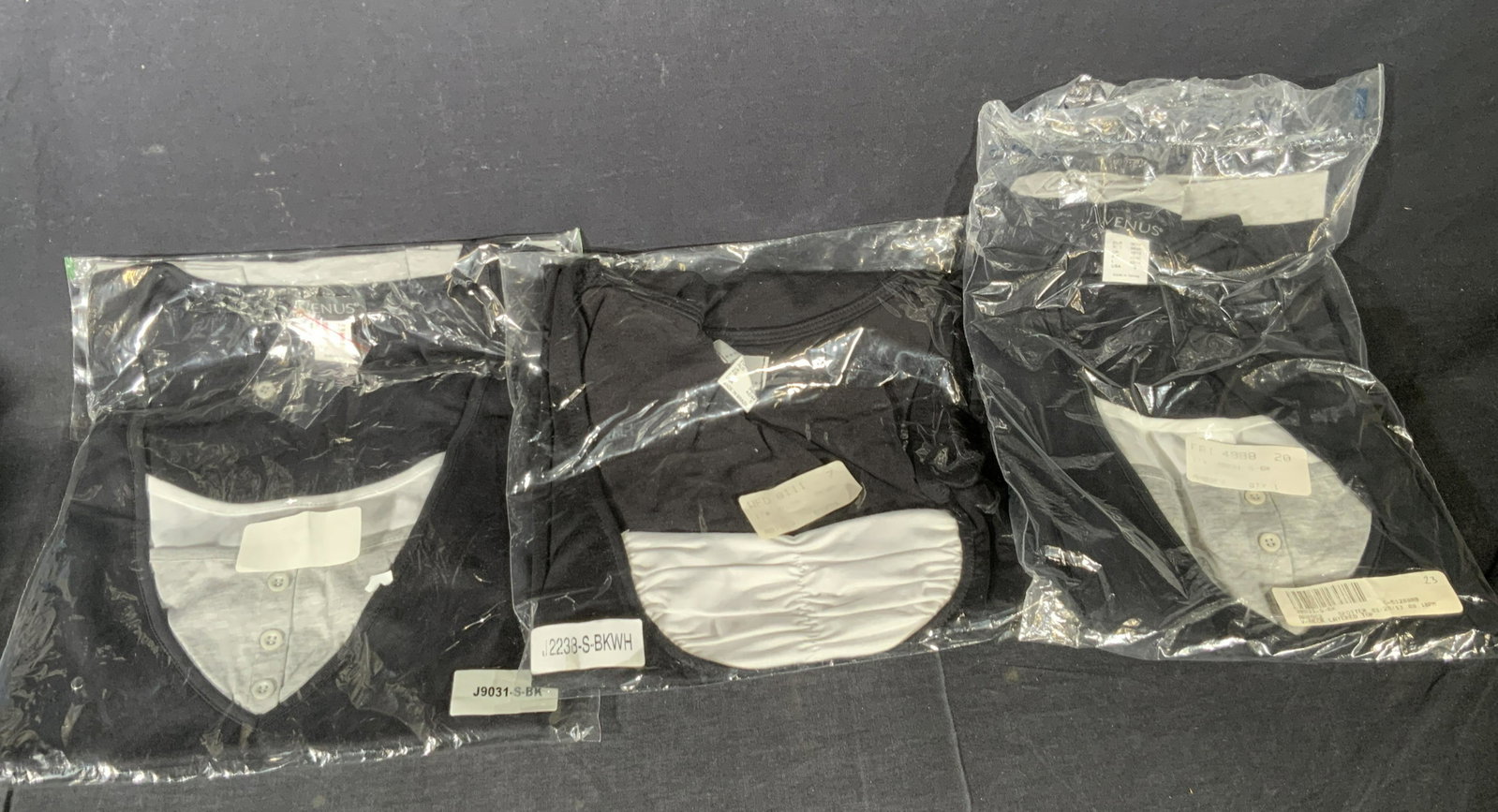 Lot 3 New In Package Ladies Tops, VENUS & More: Never Worn, New In Package black, white, and gray hued ladies tops. The tags read: Venus, USA 6 and Fashion B.P.C, USA S. Packages contain women’s tops. One Venus package reads: V-Neck Layered Top. 
