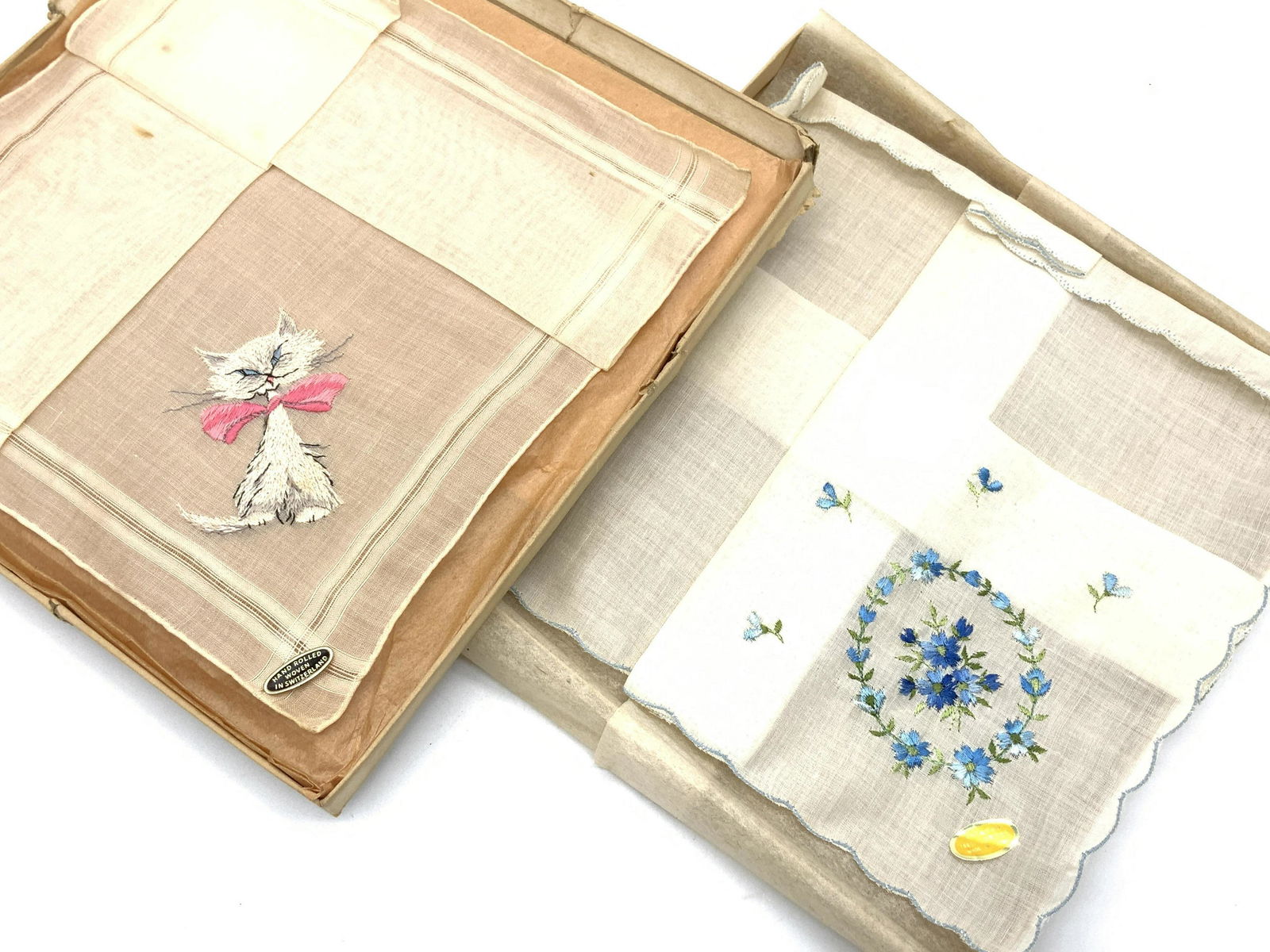 Vintage Embroidered Hankies in Org Boxes: Hand rolled Sheer silk with corner embroidered cat with large pink bow. Original sticker reads ‘Hand Rolled, Woven in Switzerland’ 11.5 in. Blue Floral Wreath Embroidery on corner of sheer cotton,