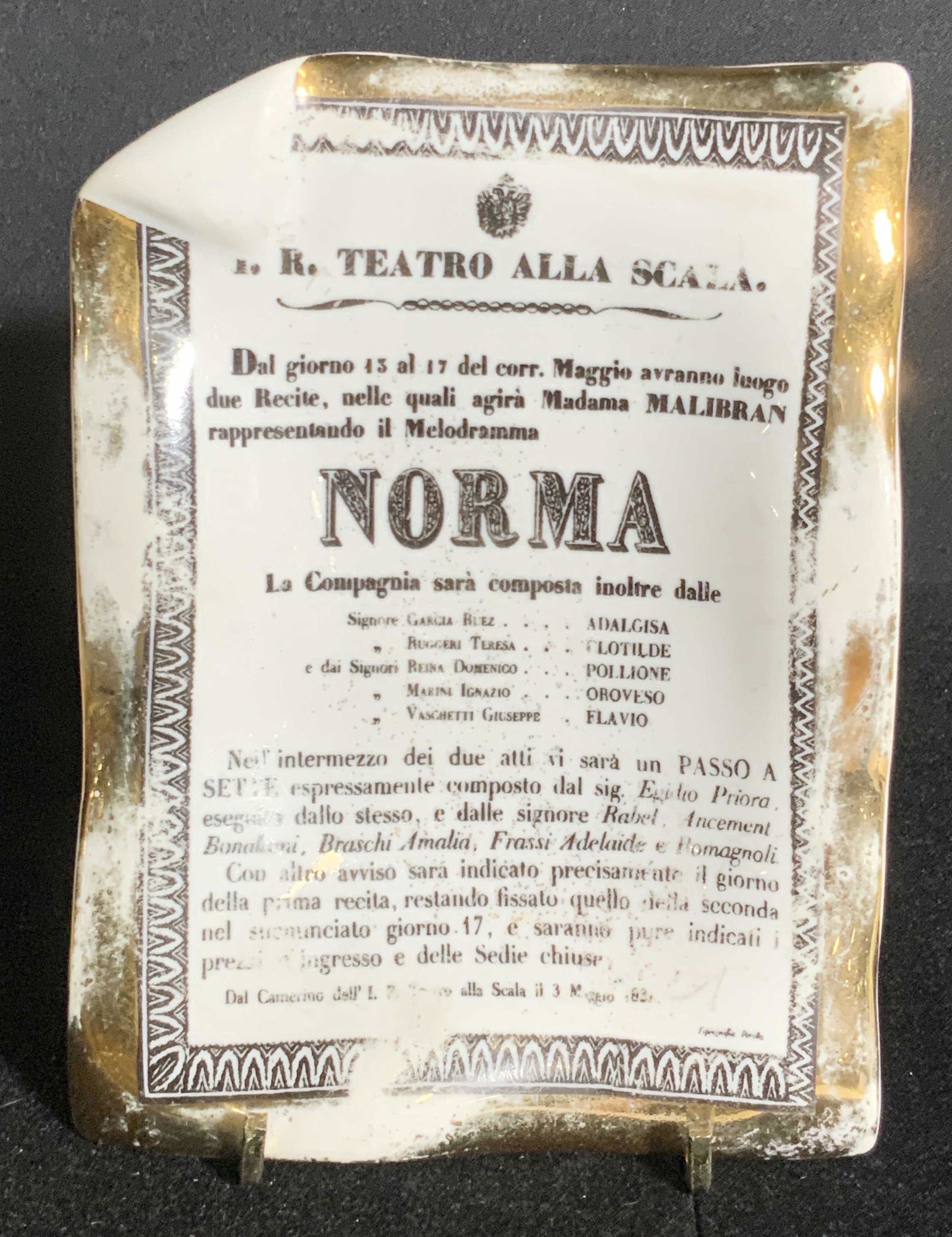 FORNASETTI Signed Italian Porcelain Norma Dish: A white porcelain keepsake/ trinket dish depicting the print image of newsprint style clipping and a gilt rim. Rim has a slight ruffle. Crafted from thick walled porcelain. Some wear to the paint. The