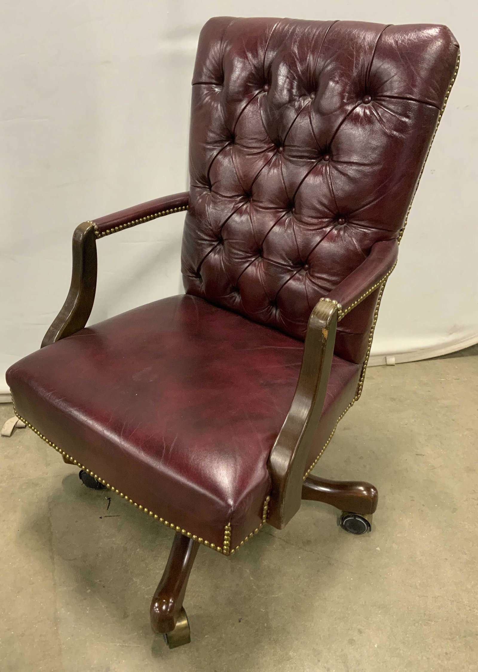 Vintage Leather Office Chair w Casters: Vintage office chair, leather, plum toned. Secured to frame with brass nails. Back is tufted. Wear is consistent with age and use. One of the wheels are damaged and needs addressing. Measures approx 3