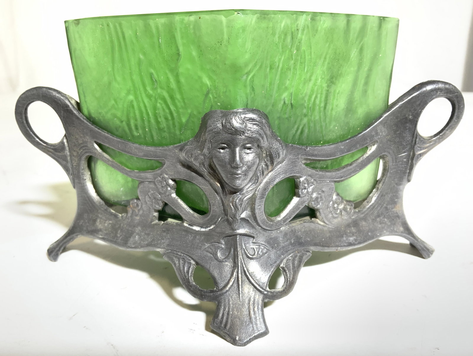 Art Glass Vessel W Footed Metal Holder: Vessel is green toned & glass. Piece is diamond shaped. Vessel sits in a dark silver toned footed holder. Front & back of piece have female head detail. Piece when put together measures approx 6 inche