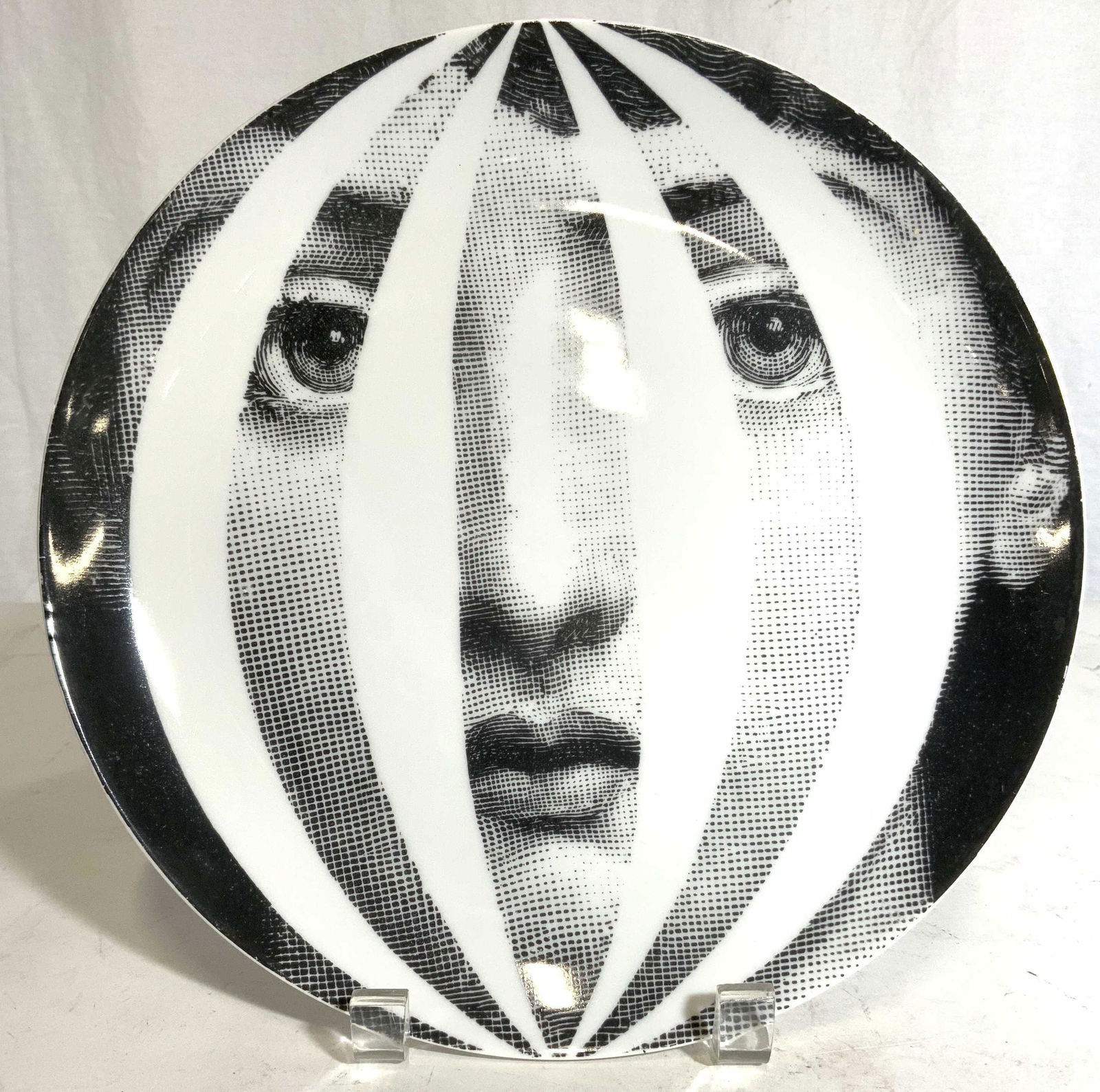 FORNASETTI MILANO Porcelain Plate: Underside of plate reads TEMA E VARDIAZIONI FORNASETTI MILANO MADE IN ITALY. Top side of plate depicts female figure portrait in black & white. Piece measures approx 10 inches wide. FORNASETTI plate,