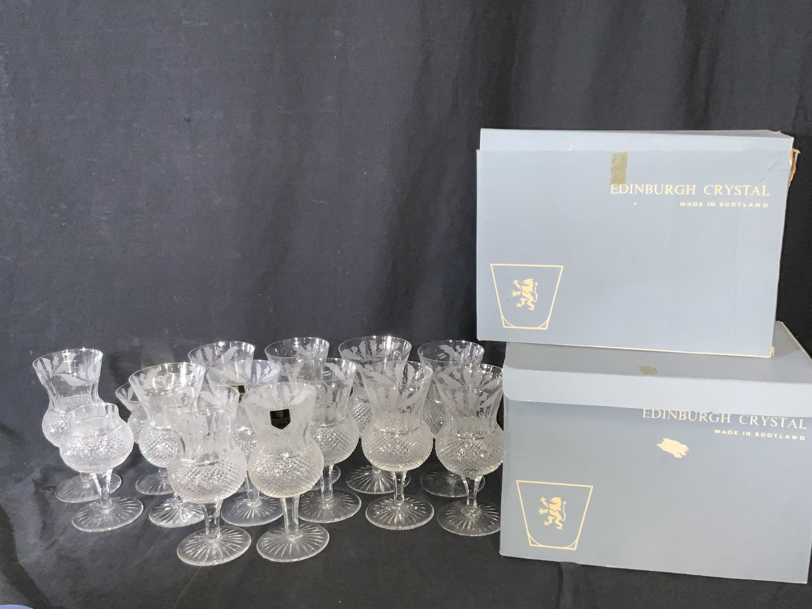 14 Boxed EDINBURGH Scottish Cut Crystal Stemware: A set of fourteen hand cut lead crystal stemware glasses and goblets. 12 pieces are taller than the other two and feature frosted foliage accents and flared rims. The other two glasses are stouter. Bo