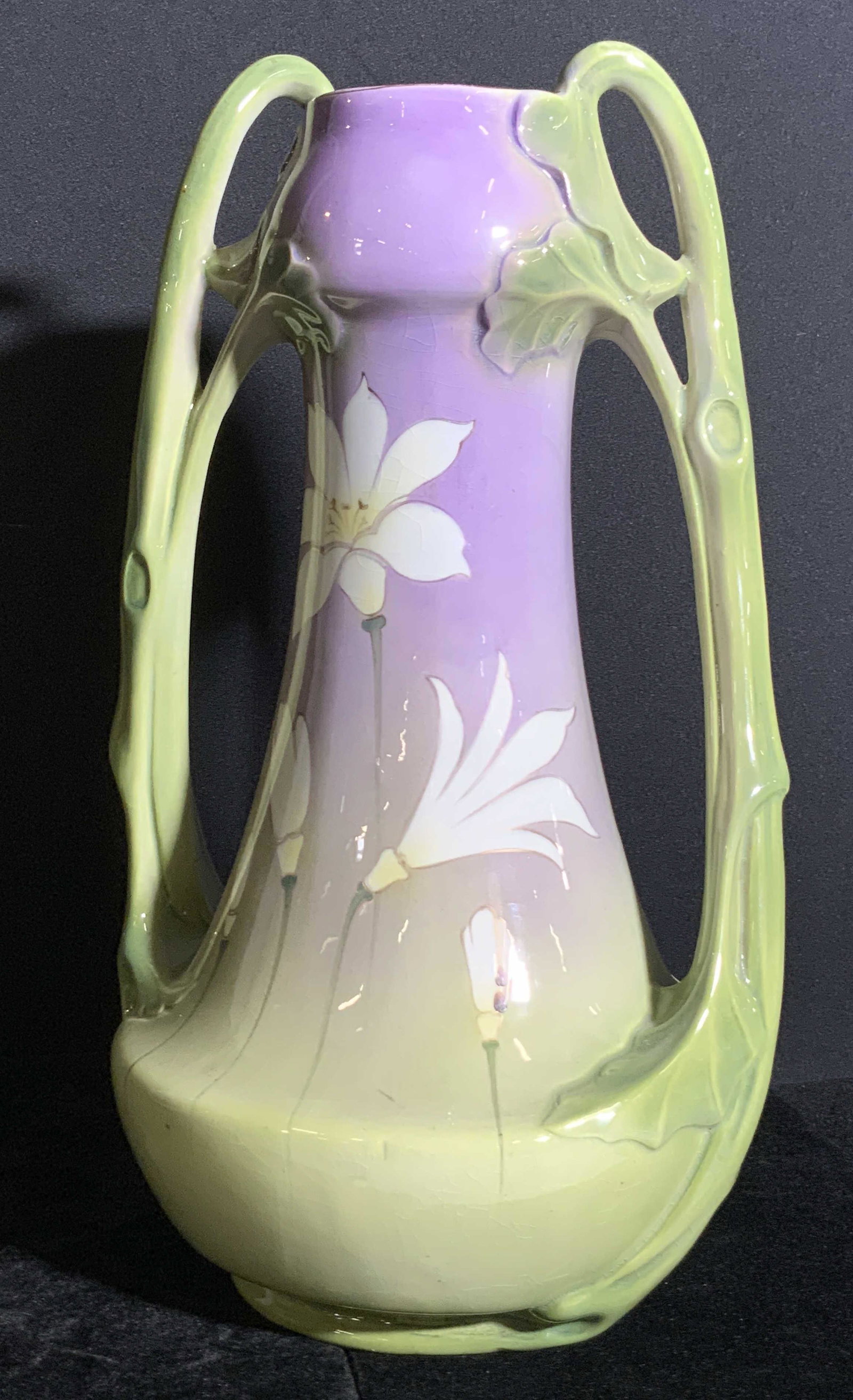 Signed Handmade French Porcelain Floral Vase: A handmade signed French porcelain floral vase. The piece is primarily purple, green, and white hued. Ombré design. Raised porcelain accents adorn the twin handles that bear leaf motifs. The undersid