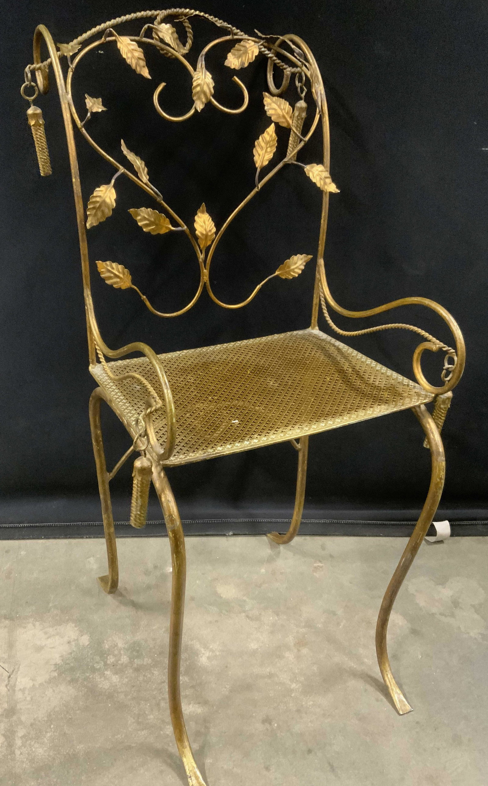 Vintage Gilded Wrought Iron Chair: Gilded wrought iron chair, vintage, possibly antique. Back is decorated with leaves, vines are arranged in a heart shaped pattern. Arms and each side of the back are decorated with metal tassel formed