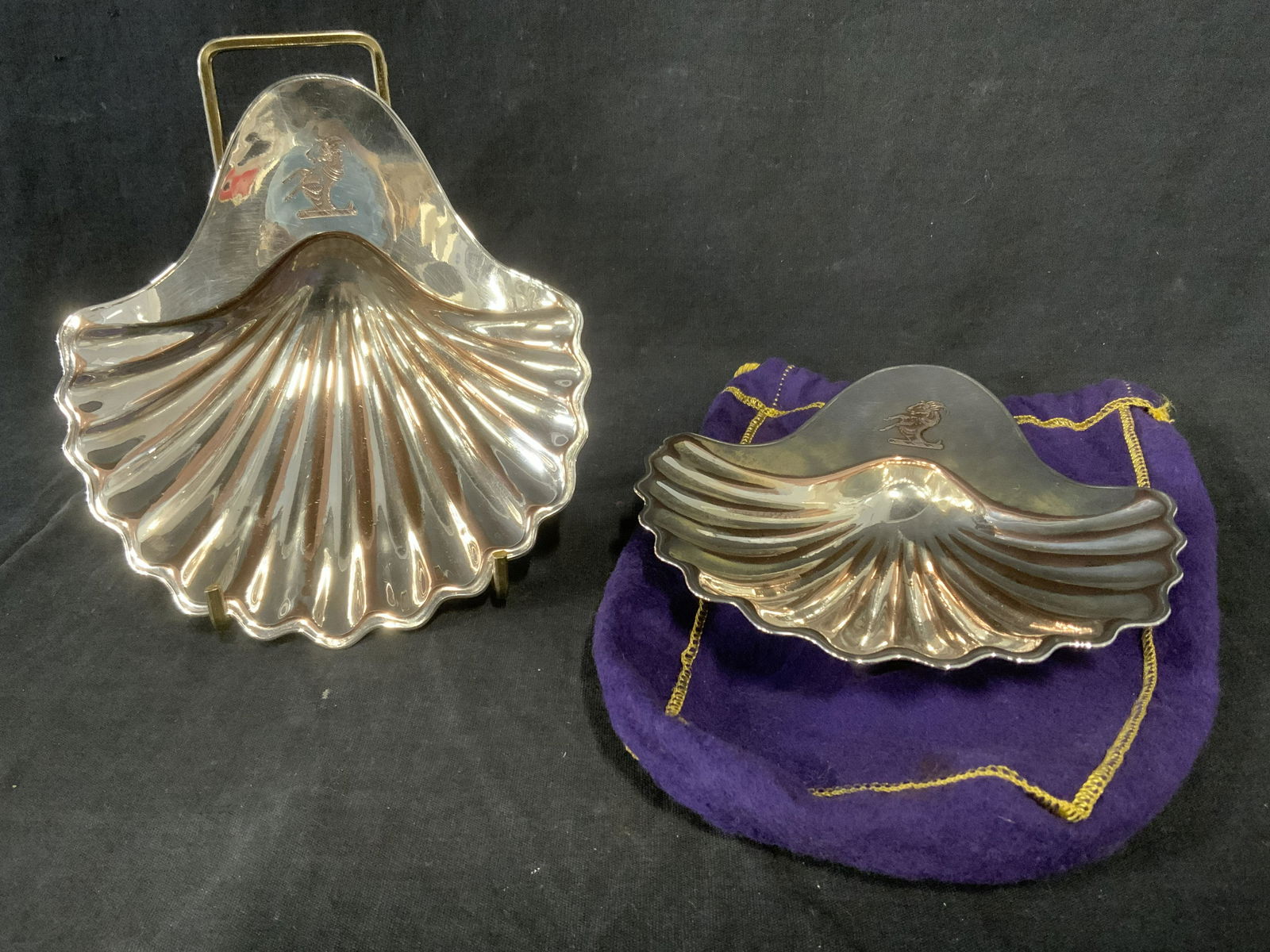 Pair SEAGRAM’S Metal Dishes: Pair of trinket dishes by SEAGRAMS, possibly vintage. Each resembles a scallop shell, an engraving resembling a goat decorates topside of dish, underside reads as SHEFFIELD, MADE IN GT BRITAIN. Includ