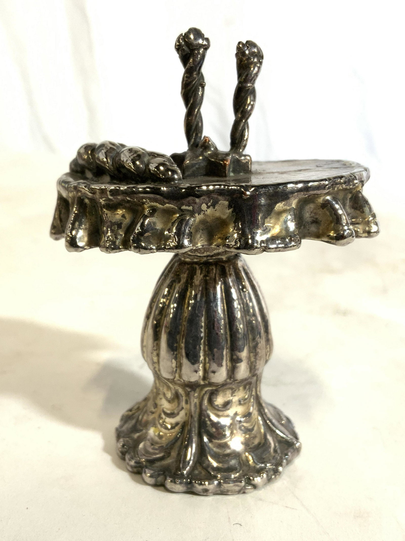 Silver Toned Metal Pedestal Table Figure: Table figure is silver toned & metal. Piece is pedestaled with oval top. Top of piece has candlestick structure. Underside has green toned felt. Piece measures approx 3.5 inches tall 2.5 inches wide, 