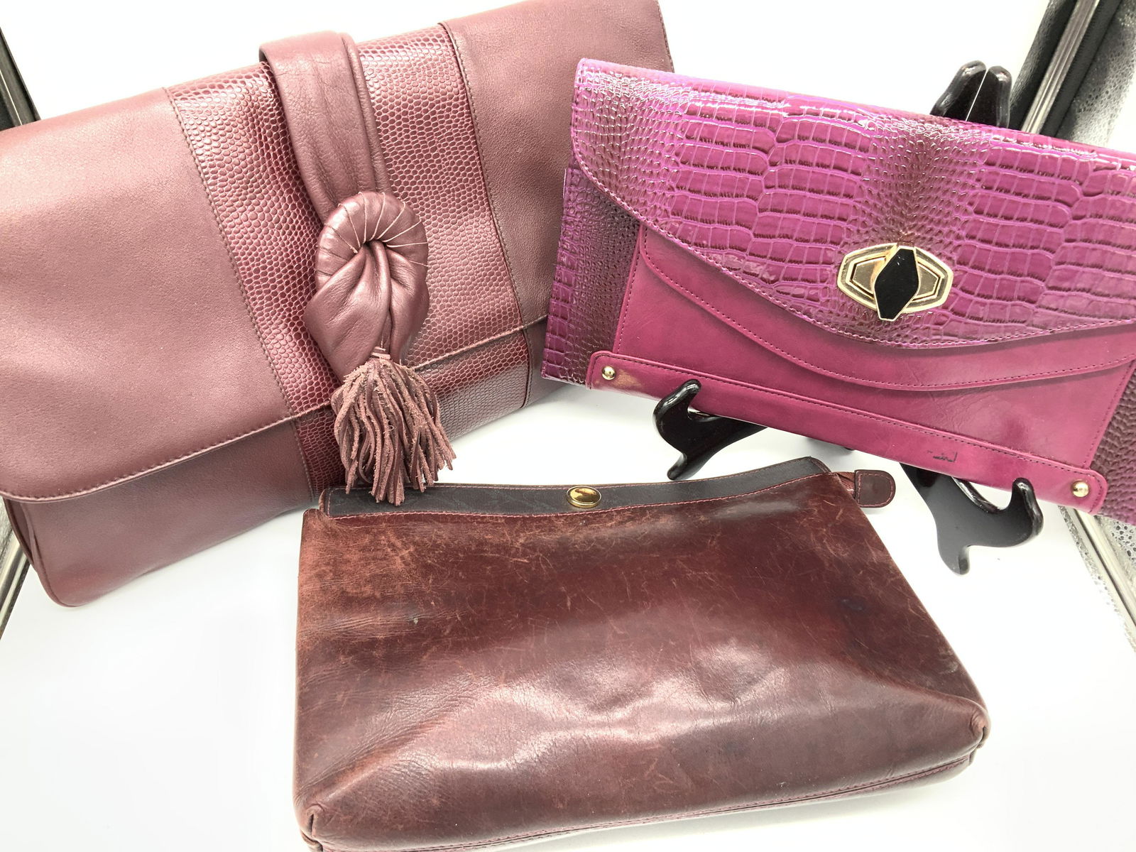 Lot 3 Vintage Leather Clutches, Movado and More: Lot of 3 leather or leatherette clutches all in hues of eggplant. Two unmarked. SIGNED label vintage MOVADO MADE IN ITALY, zipper closure with signed zipper clasp, I inner zippered pocket, wear to lin