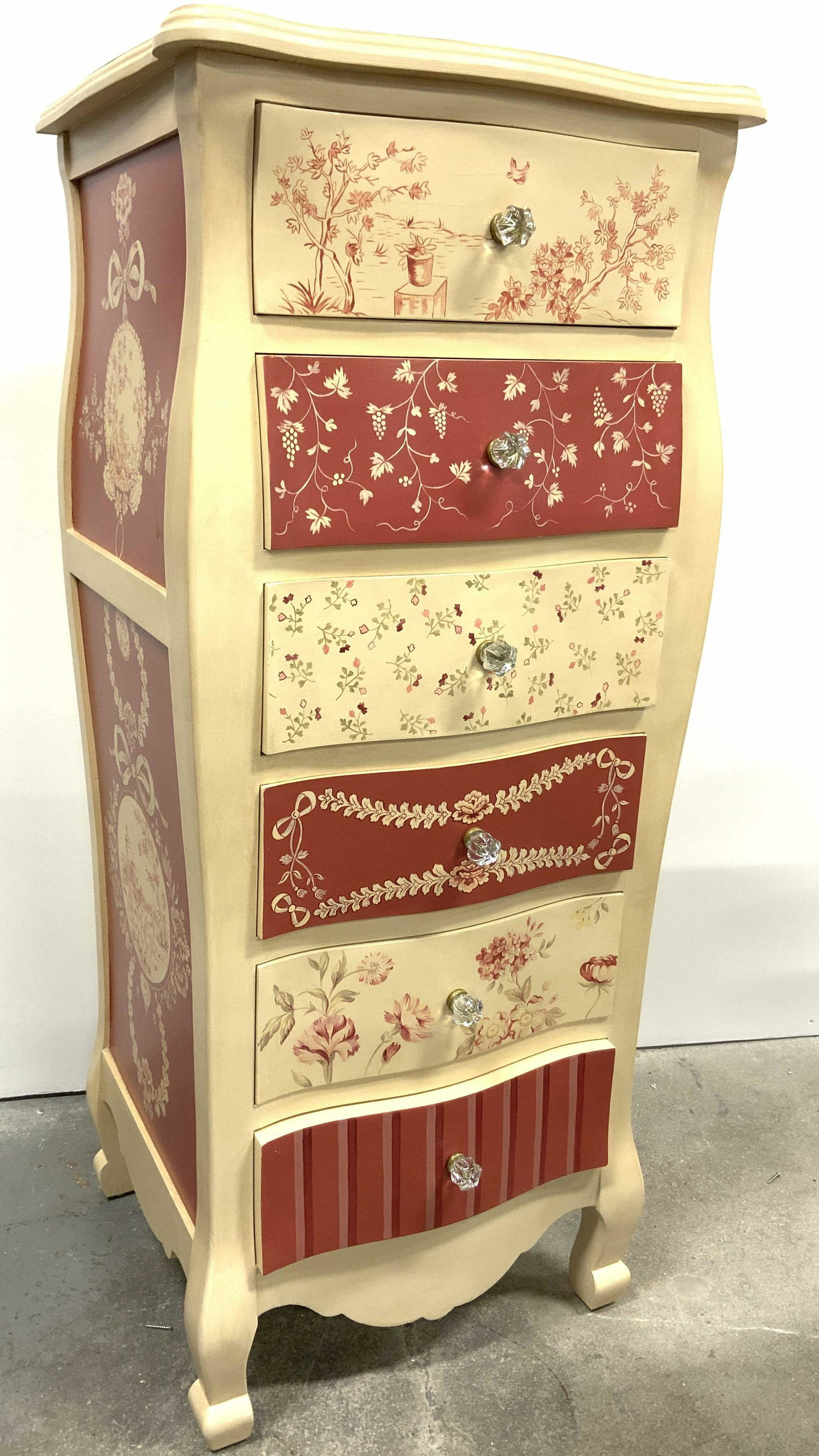5 Drawer Wooden Lingerie Chest Of Drawers: Chest includes 5 drawers. Piece appears to be wooden possibly veneer. Each have which appear to be glass possibly lucite. Each drawer has floral & leaf detail, lowest drawer has striped detail. Piece 