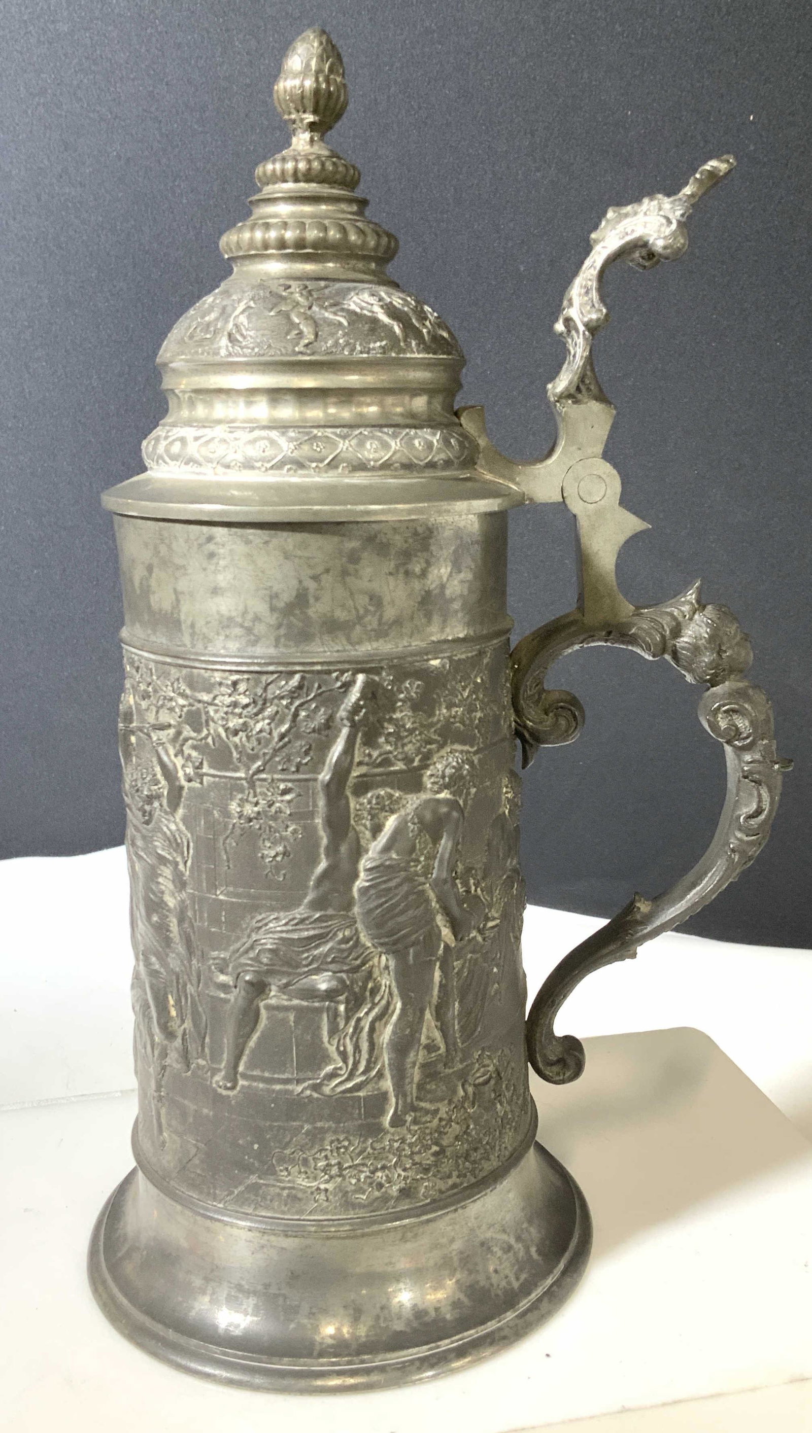 Collectible Embossed Metal Tankard Stein: Vintage Collectible Stein, embossed neoclassical decor , acorn finial, depicting young Roman Servant pouring Wine and vestal virgins ( all possibly representations). Adorned with grape vine motif , mu