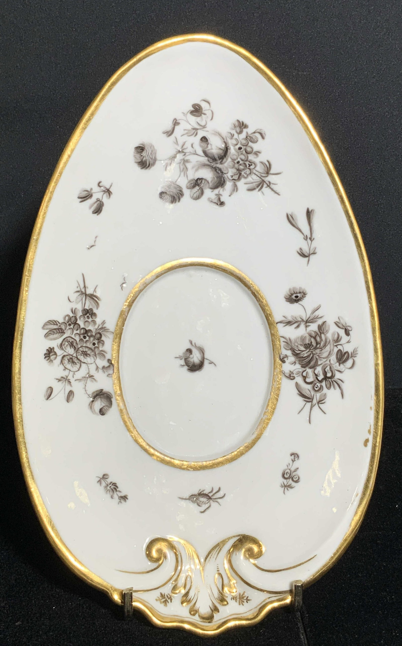 Vintage MEISSEN Trademarked Floral Porcelain Plate: A vintage white porcelain plate decorated with gilt line work and grayscale florals. Plate is egg formed in shape. Embossed porcelain accents. Underside is marked with Meissen crossed swords. Piece ha