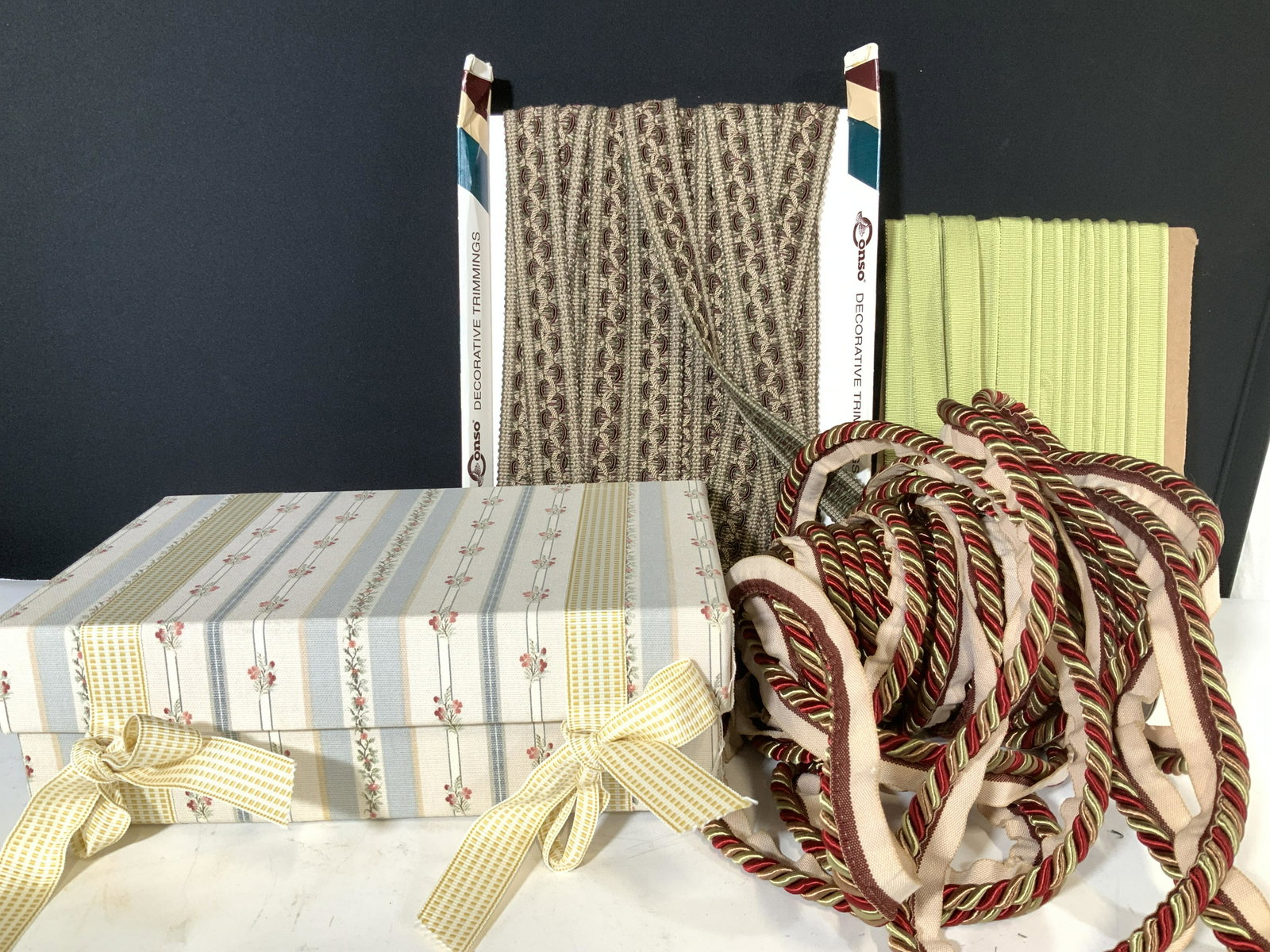Lot Calico Corners Upholstery Cording & Fabric Box: 3 types of fabric trim- flat woven trim on colors of moss green, taupe and burgundy. Enough for a pillow or two. Grass green cording, enough for a pillow, possibly two. Heavy twisted lip cord on bolt,