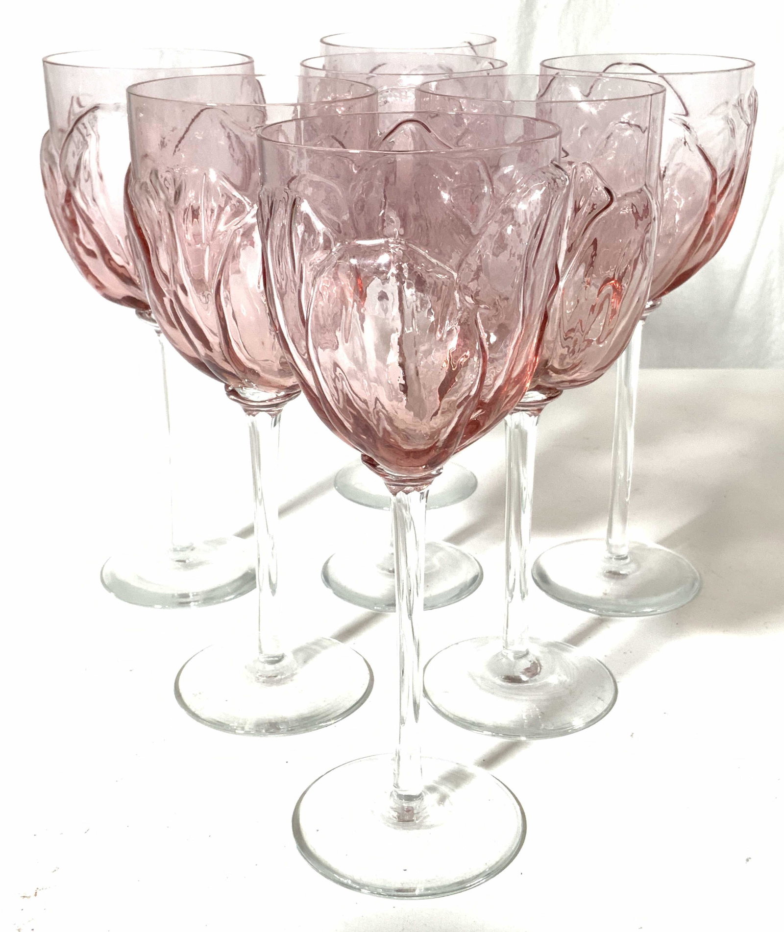 Set 7 Pink Art Glass Goblets: Lot includes 7 goblets. Each have beveled basins which resemble flowers. Each goblet has pink toned basins with clear stems. Each piece measures approx 8 inches tall 3 inches wide. Goblets, wine glass