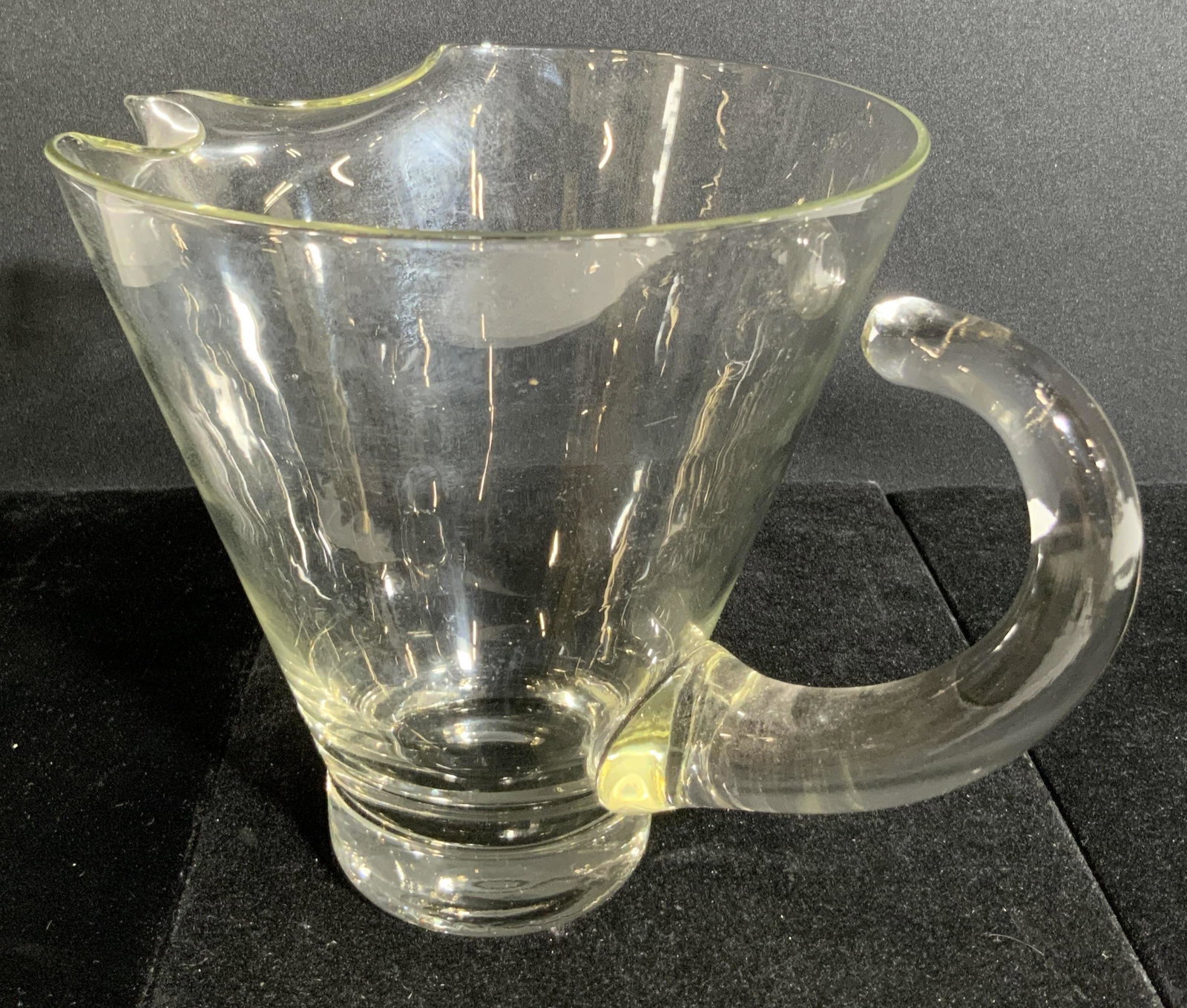 Clear Art Glass Pitcher, Kitchenware: A colorless, clear art glass pitcher with a pinched spout and detached handle. The handle is crafted from thick walled glass. Approx. 7H x 6.5W in. Some surface wear. Tabletop accessories and decor, d
