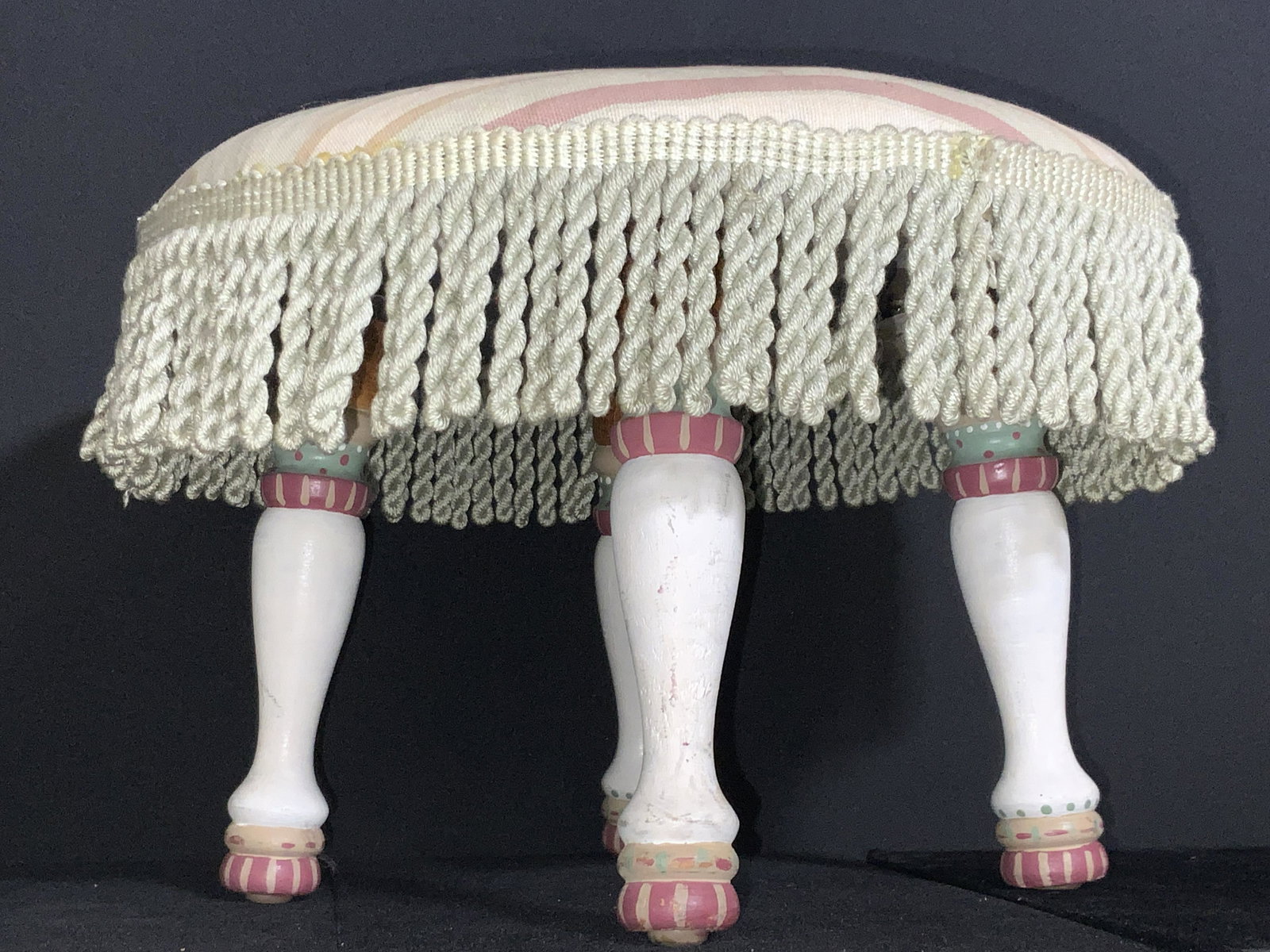 Upholstered Tassel Footstool, Home Decor: A upholstered footstool with four hand painted & carved legs. The upholstery features a muted striped pattern that edges at the edges and gives way to cascading tassels. Some wear to woodwork and upho