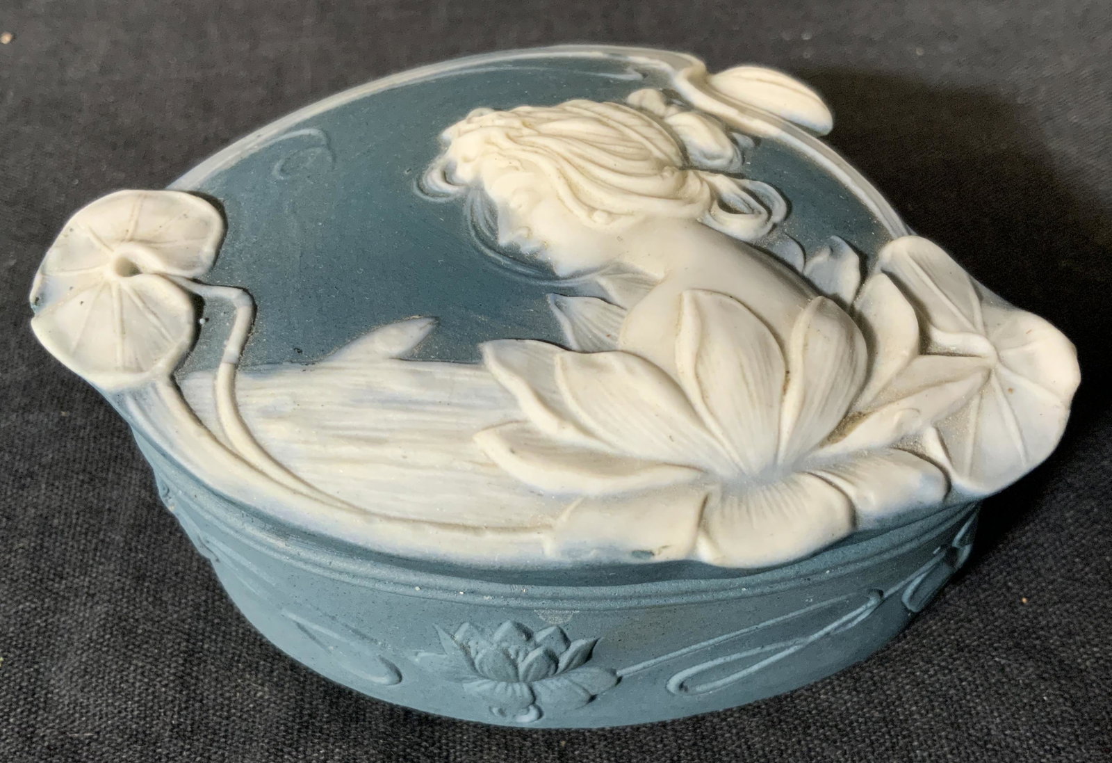 Porcelain Lidded Trinket Box: Porcelain lidded trinket box, no apparent inscriptions or markings, piece is not glazed, lid to box depicts a woman in a lake with Lilly pads and lotuses surrounding her, piece measures 1.5 inches tal